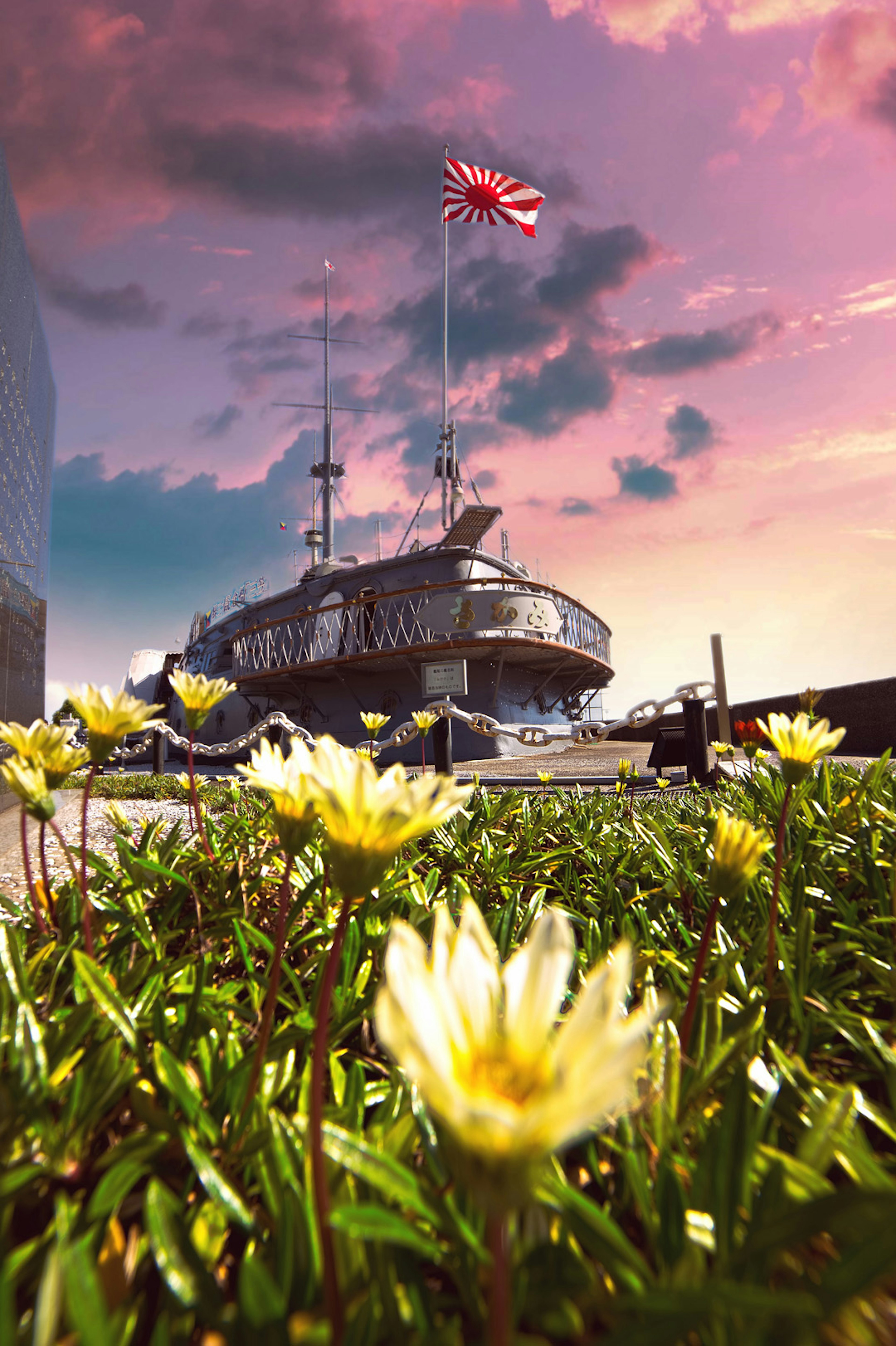 Una escena de atardecer con un barco con bandera japonesa y flores en primer plano