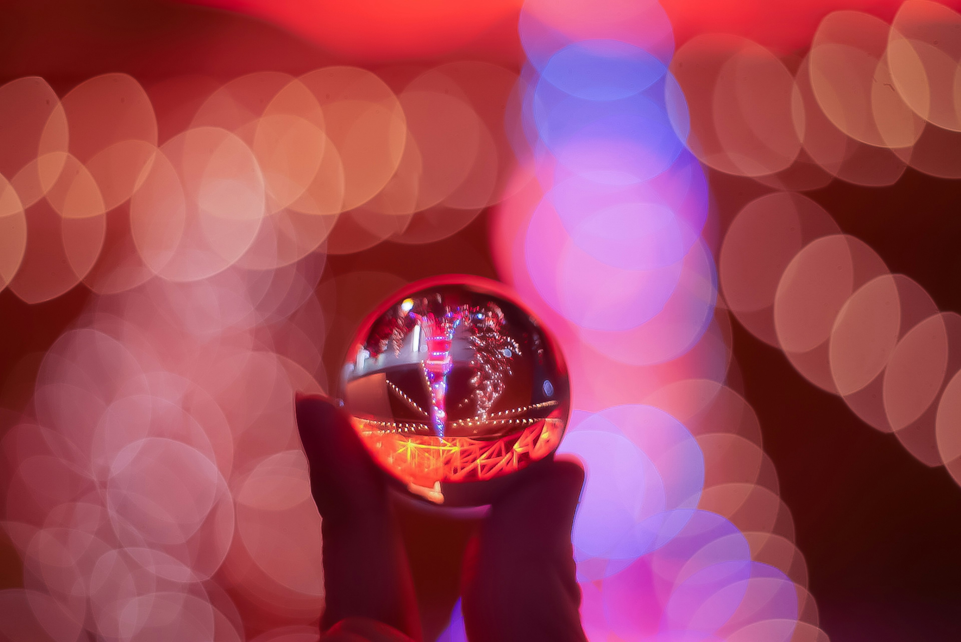 Hand holding a glass orb reflecting colorful lights in a blurred background