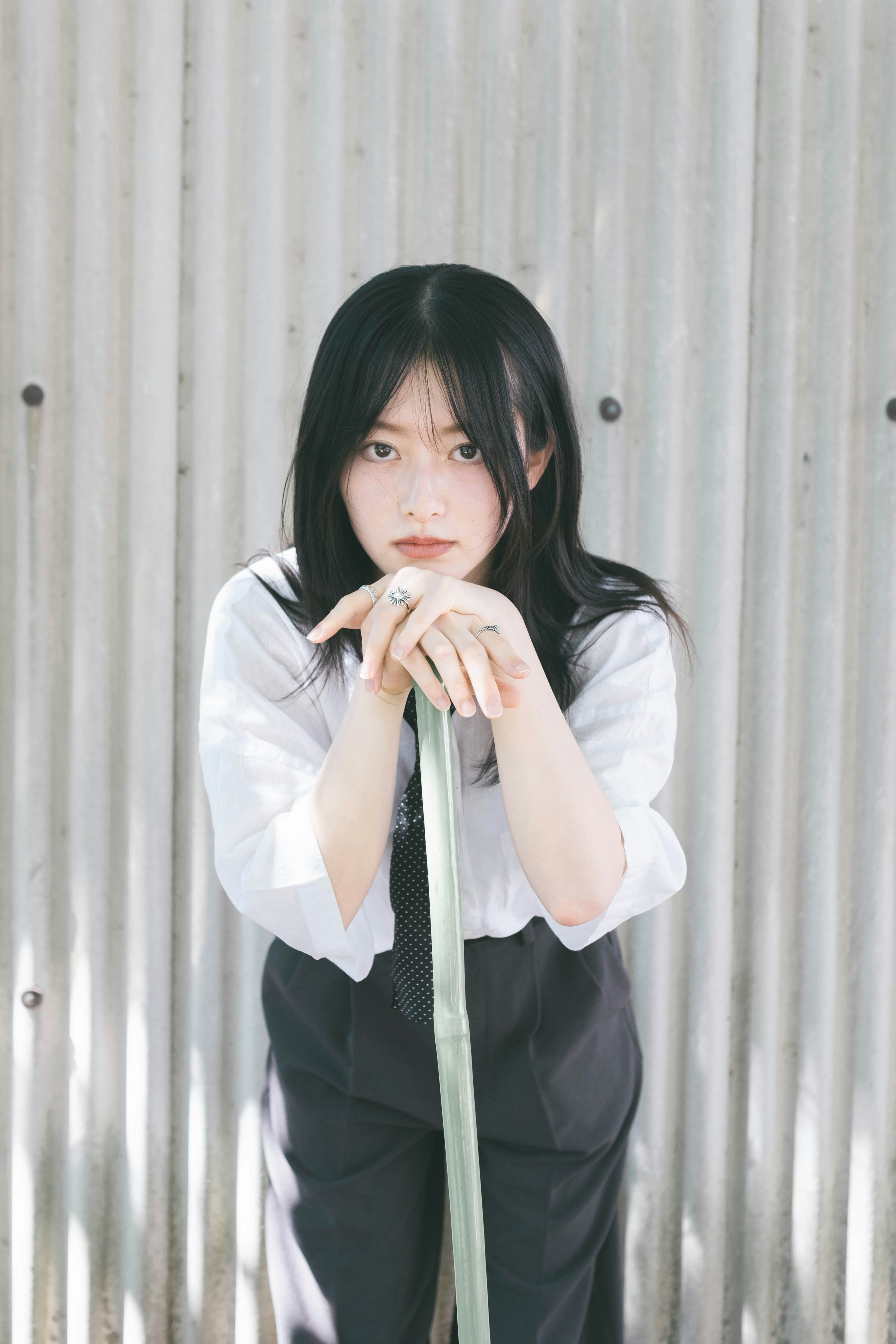 A woman with black hair wearing a white shirt stands in front of a metal background