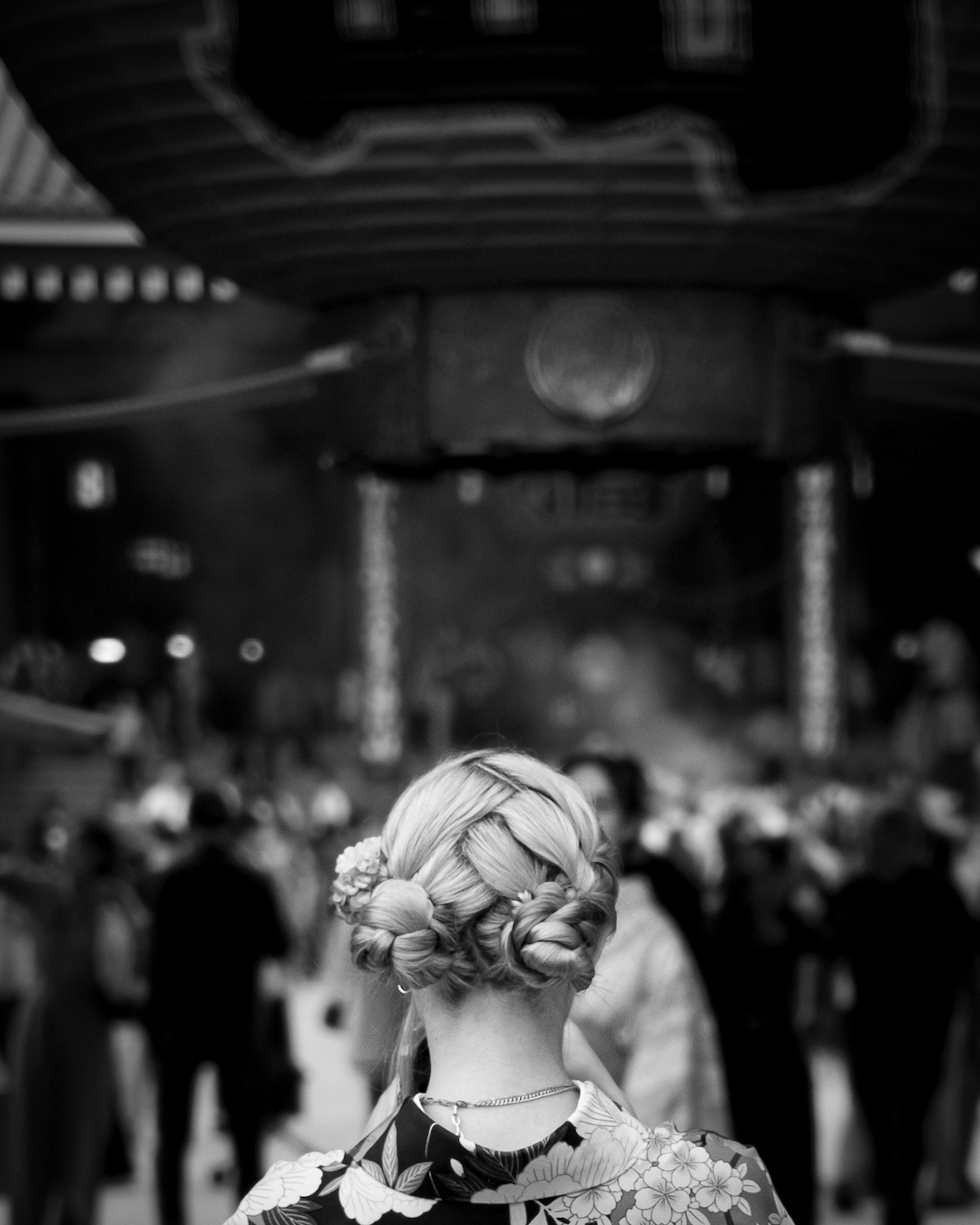 A woman's back view in black and white with braided hair and a vibrant outfit in a crowded setting