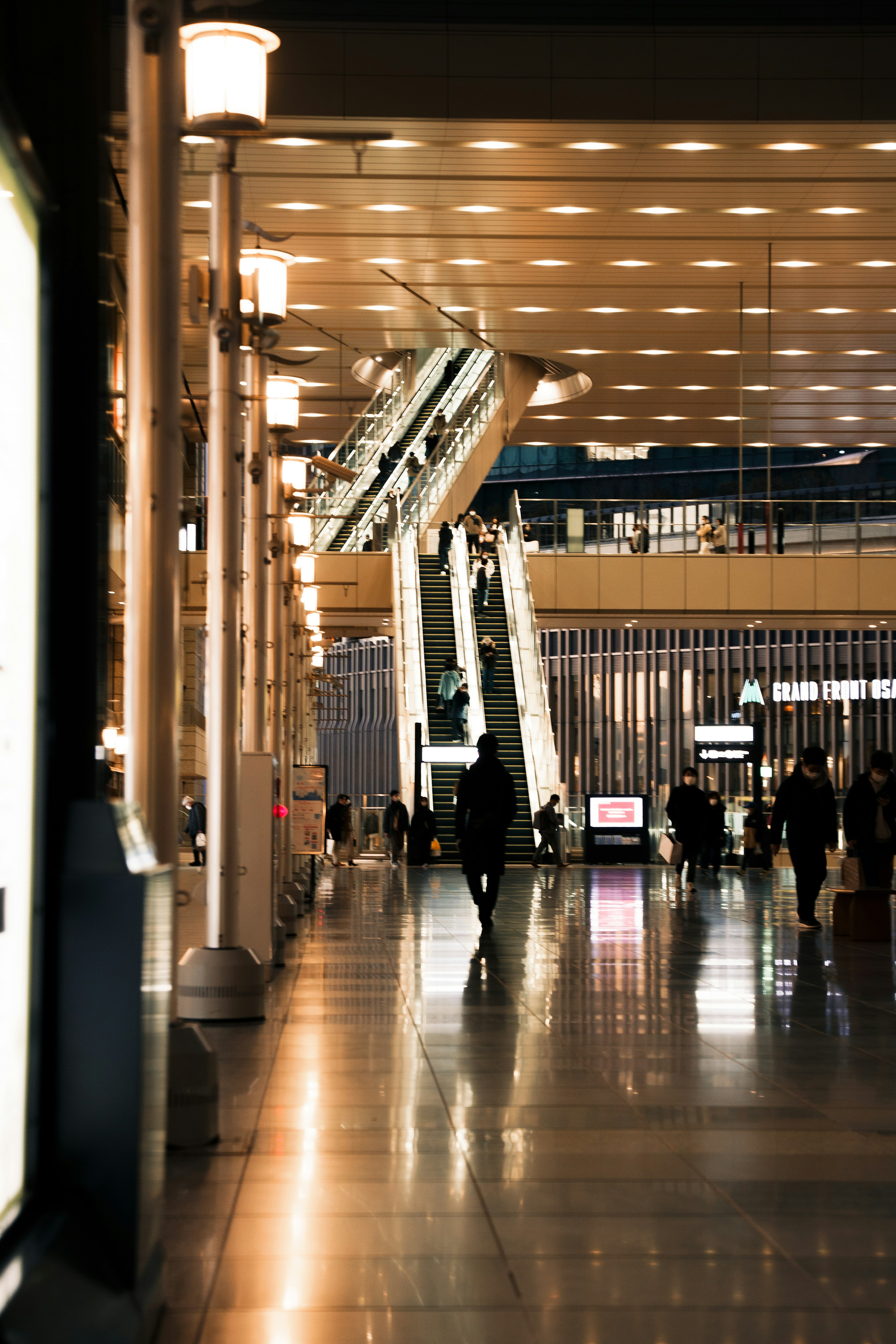 Interior of a modern building with bright lighting featuring an escalator and silhouettes of people