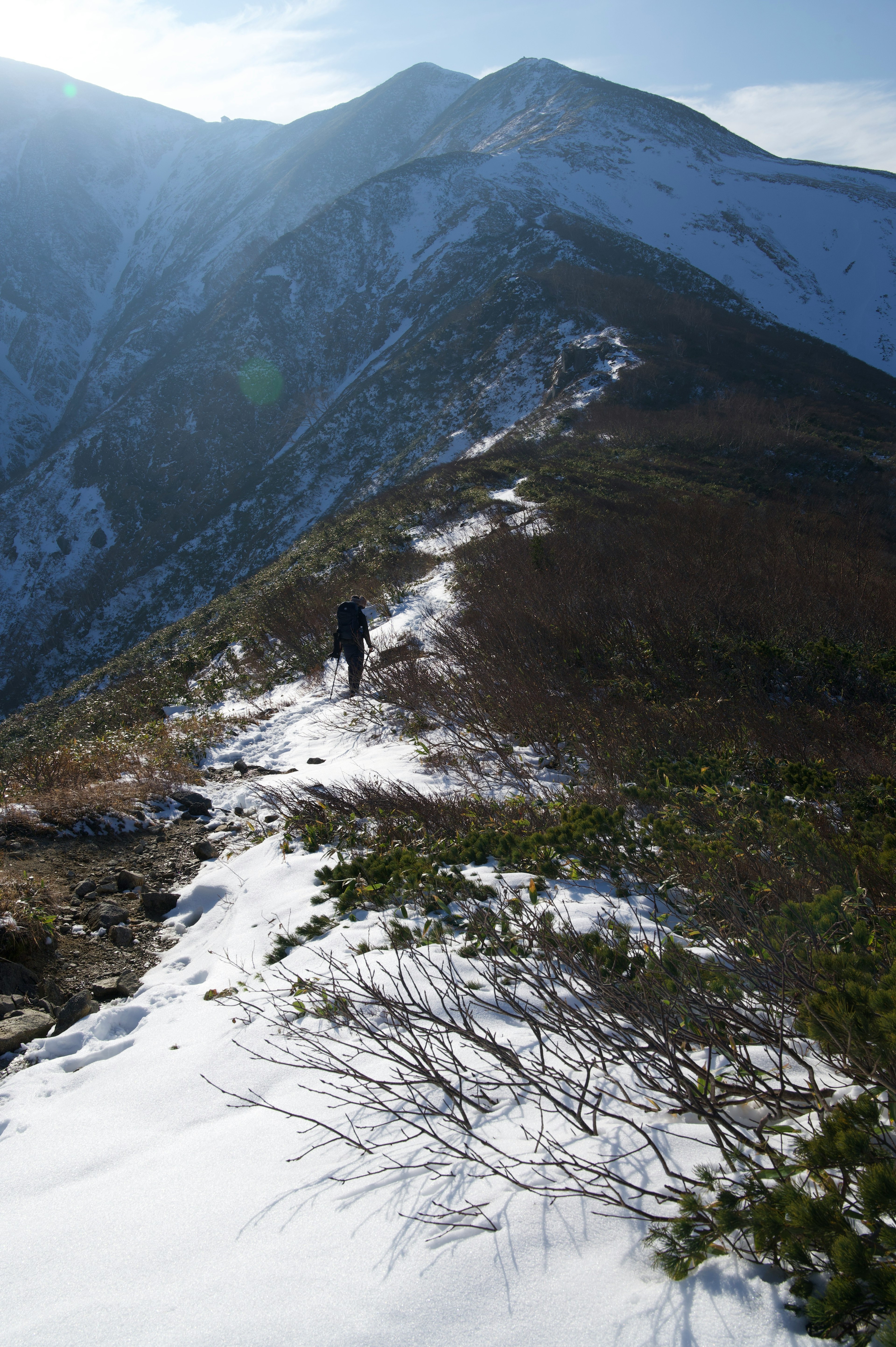 Hiker walking along a snow-covered mountain trail under blue sky