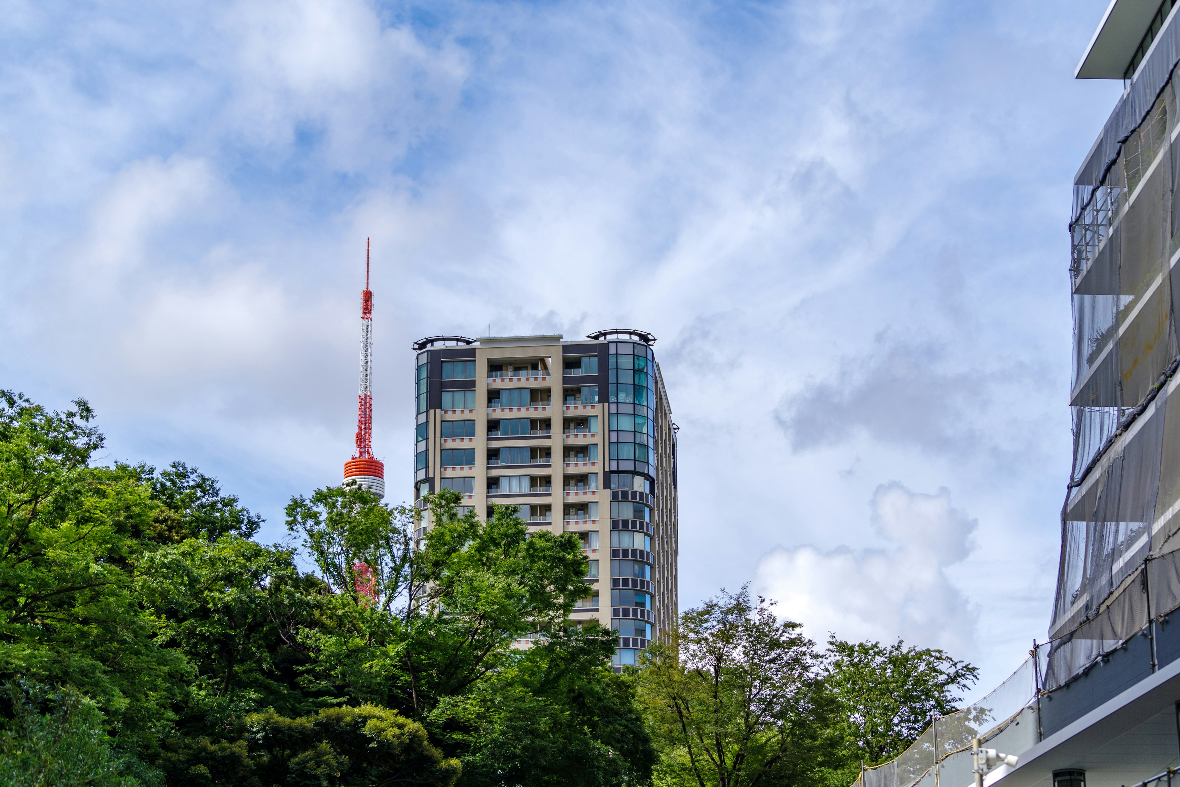 Garis langit perkotaan dengan gedung tinggi dikelilingi oleh pepohonan hijau di bawah langit biru