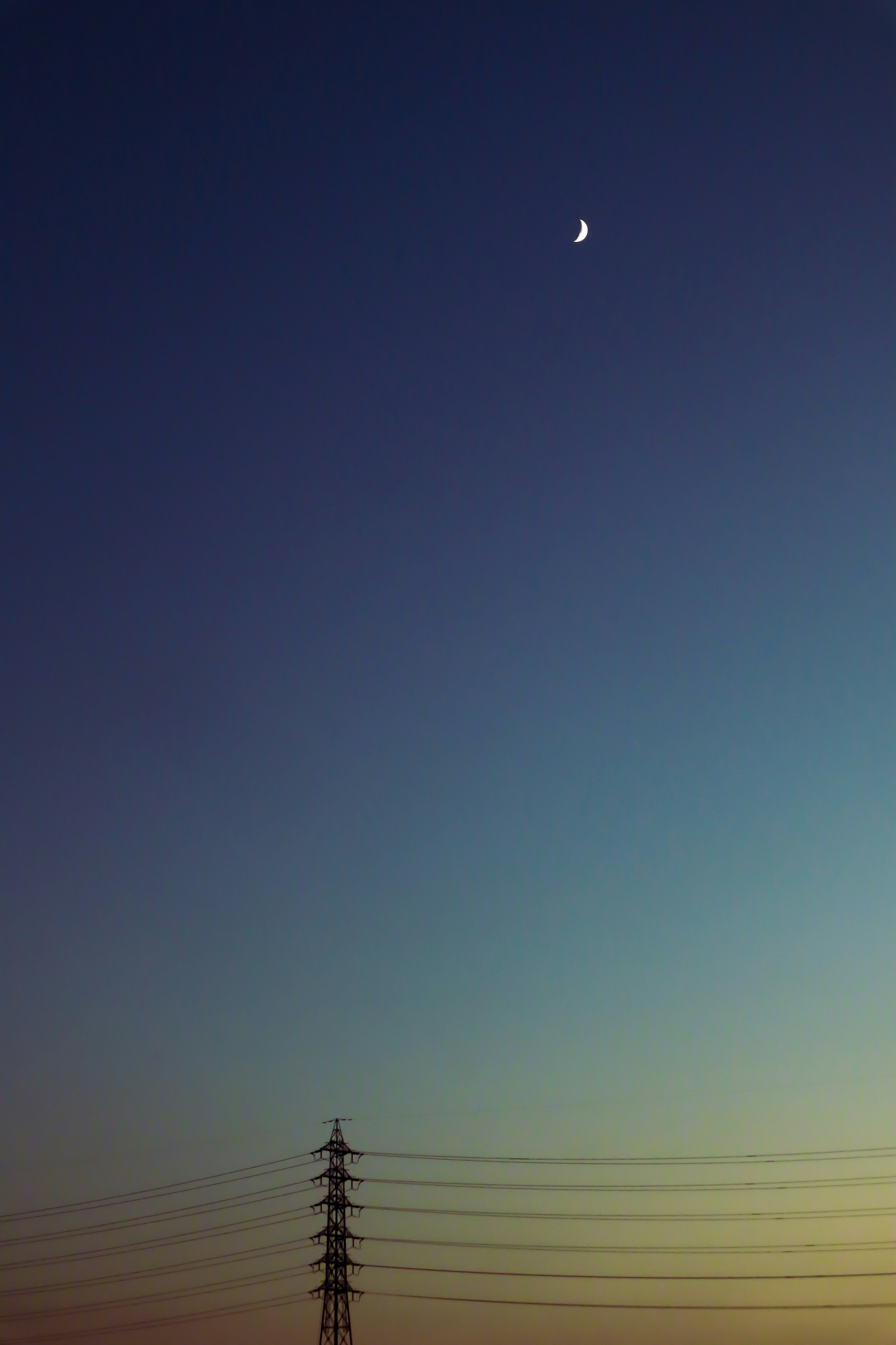 Lune croissante dans le ciel du soir avec des lignes électriques