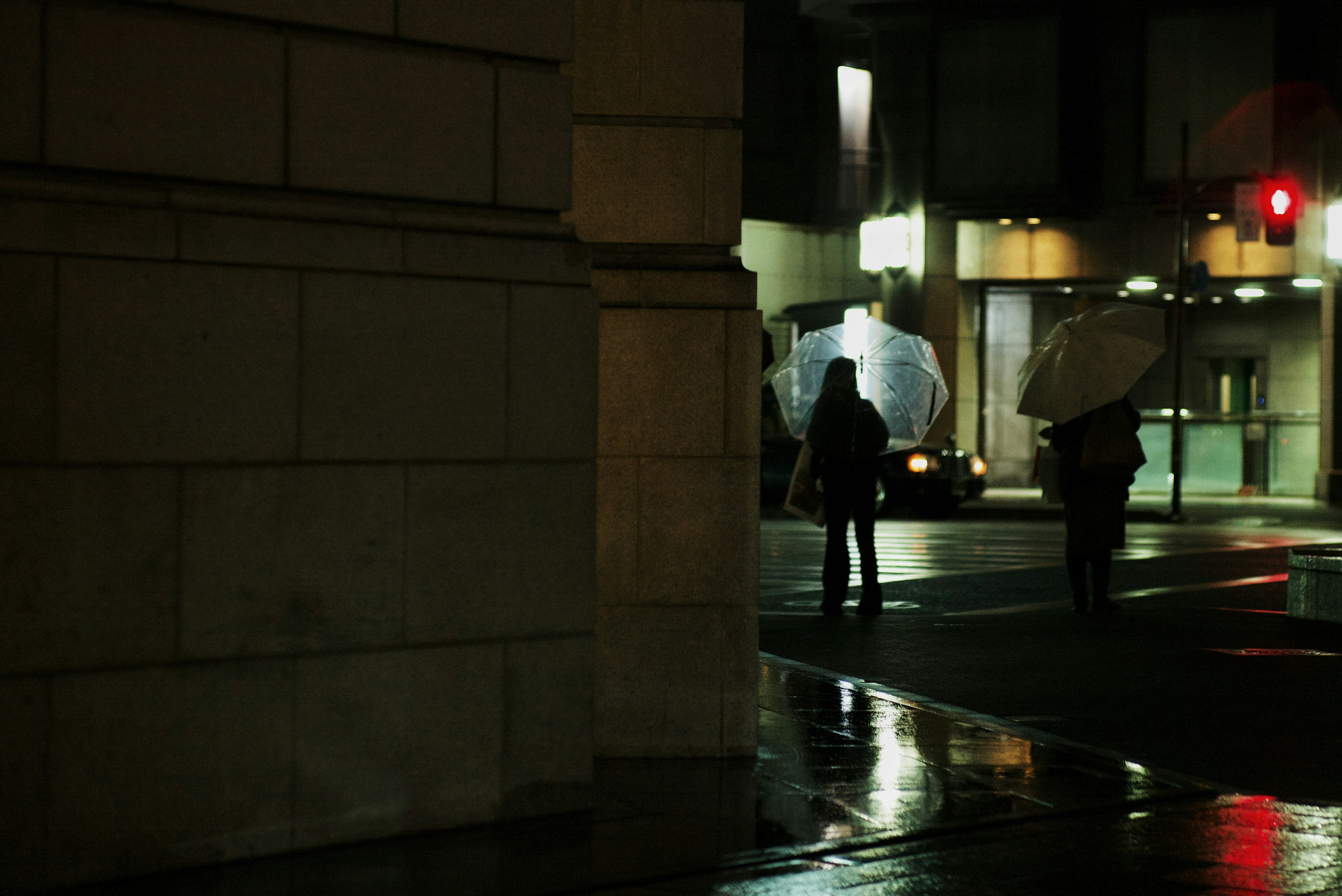 Two people holding umbrellas crossing a street at night