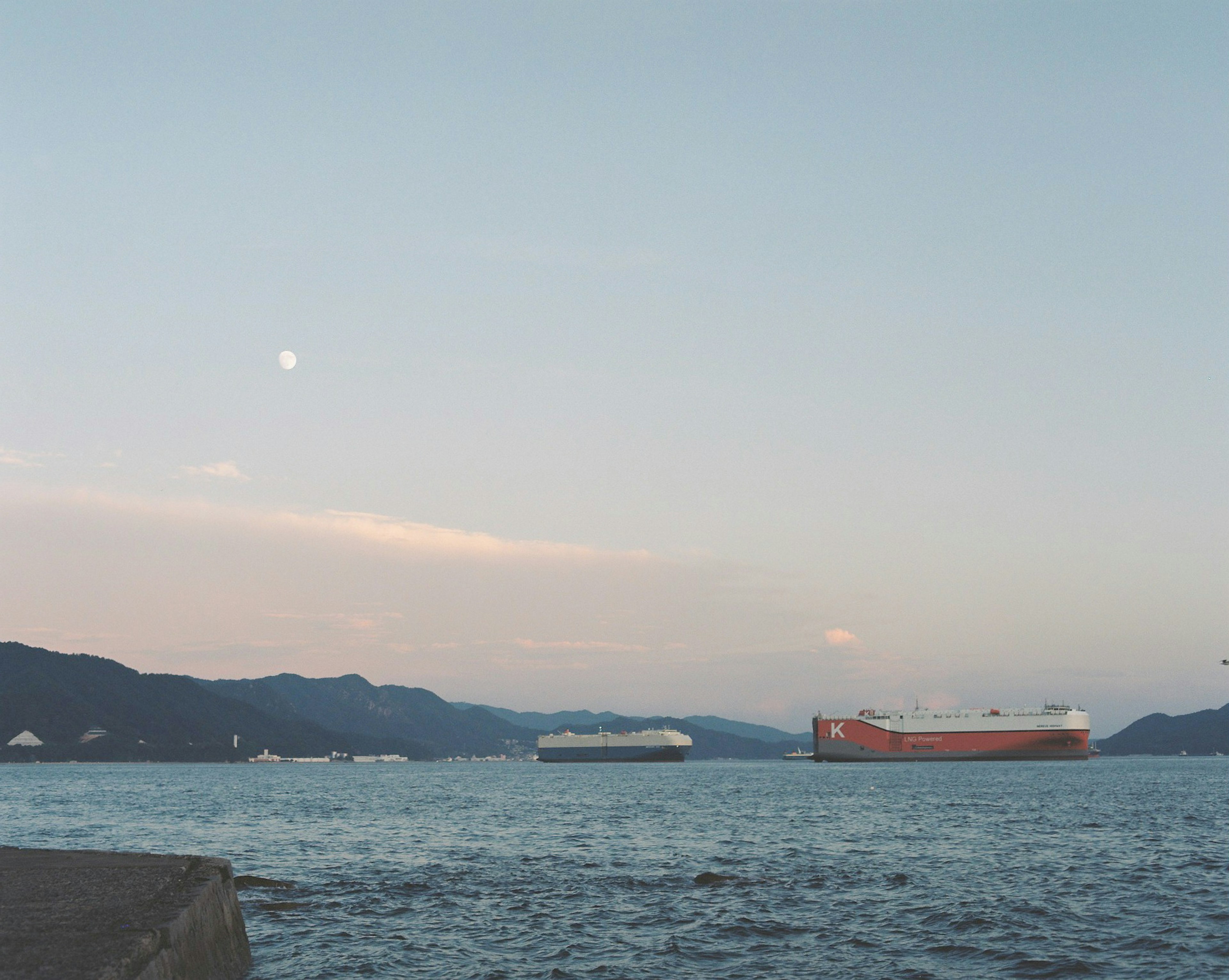 Two cargo ships on a calm sea under a serene sky with a visible moon