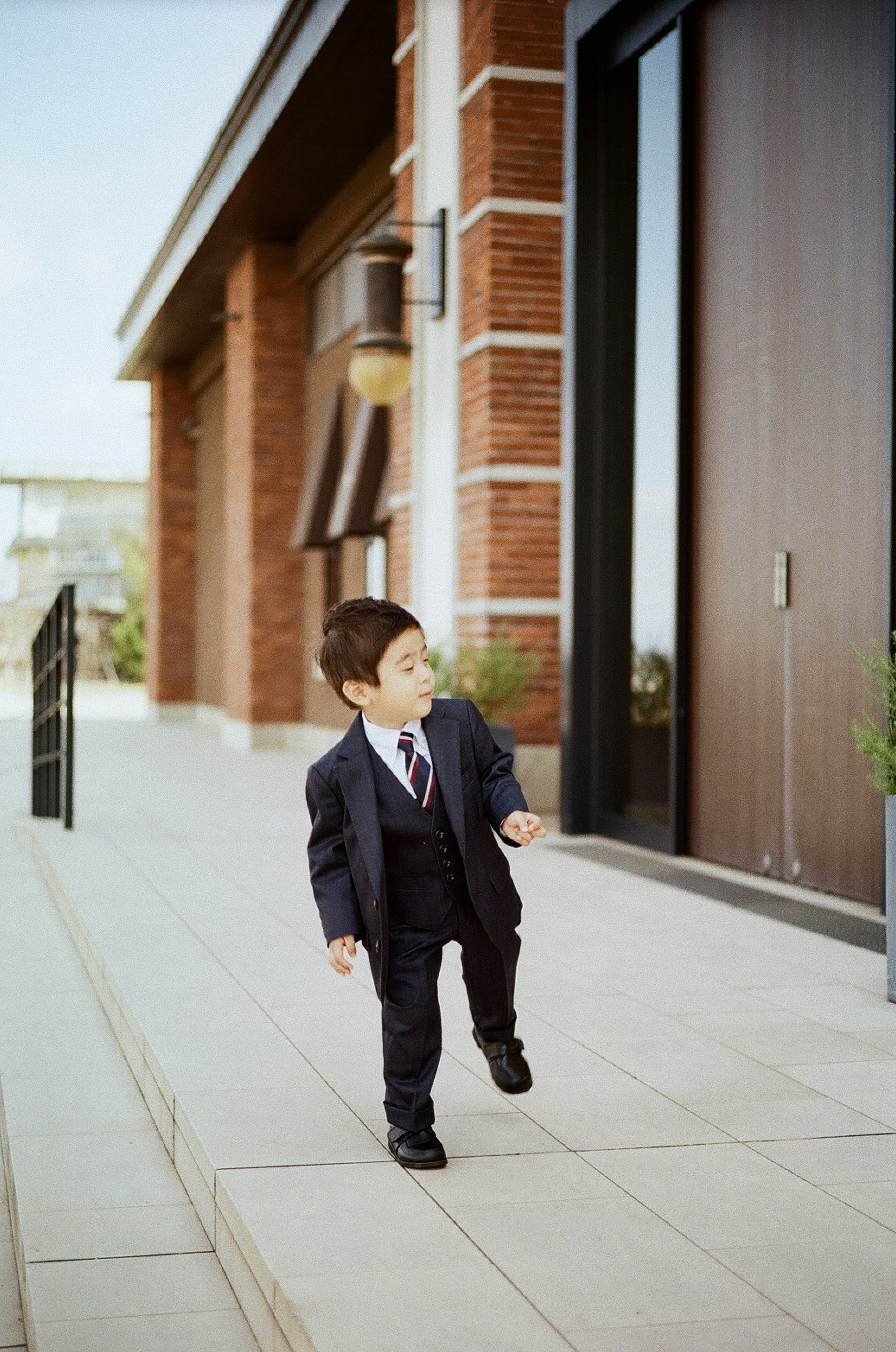 A young boy in a suit walking outside a building