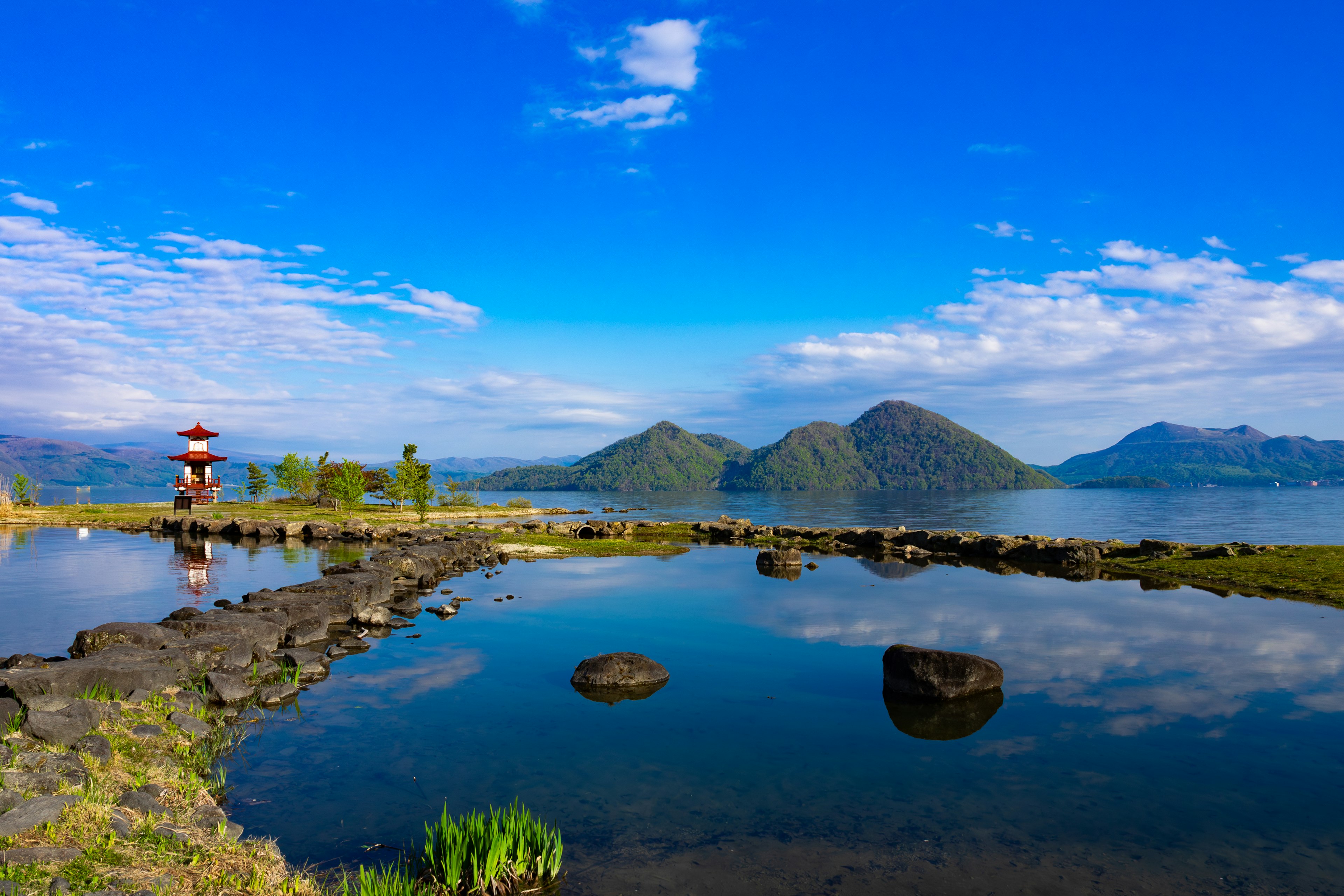 Pemandangan danau dengan latar belakang pegunungan di bawah langit biru dengan awan