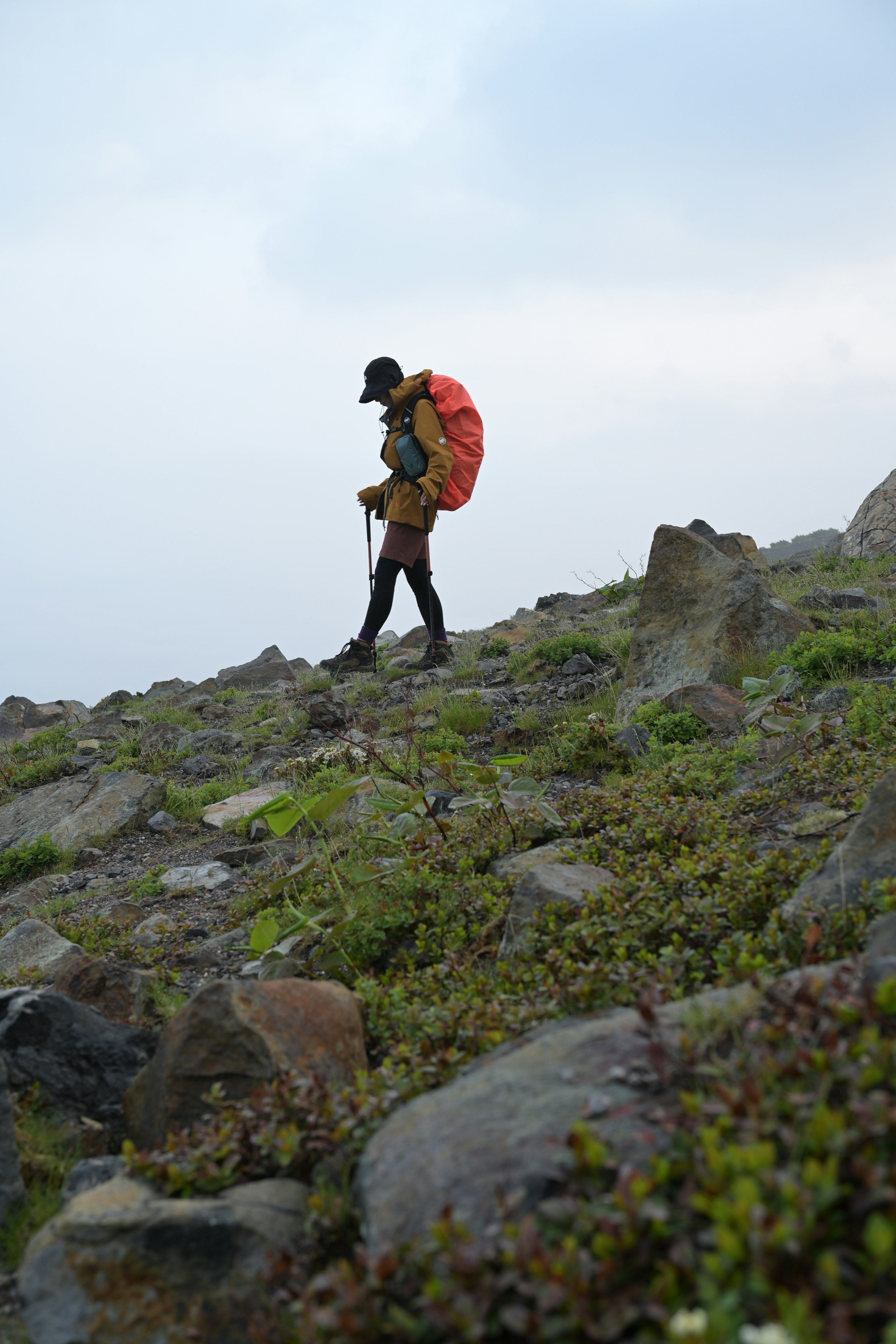 A hiker walking on a rocky slope carrying an orange backpack