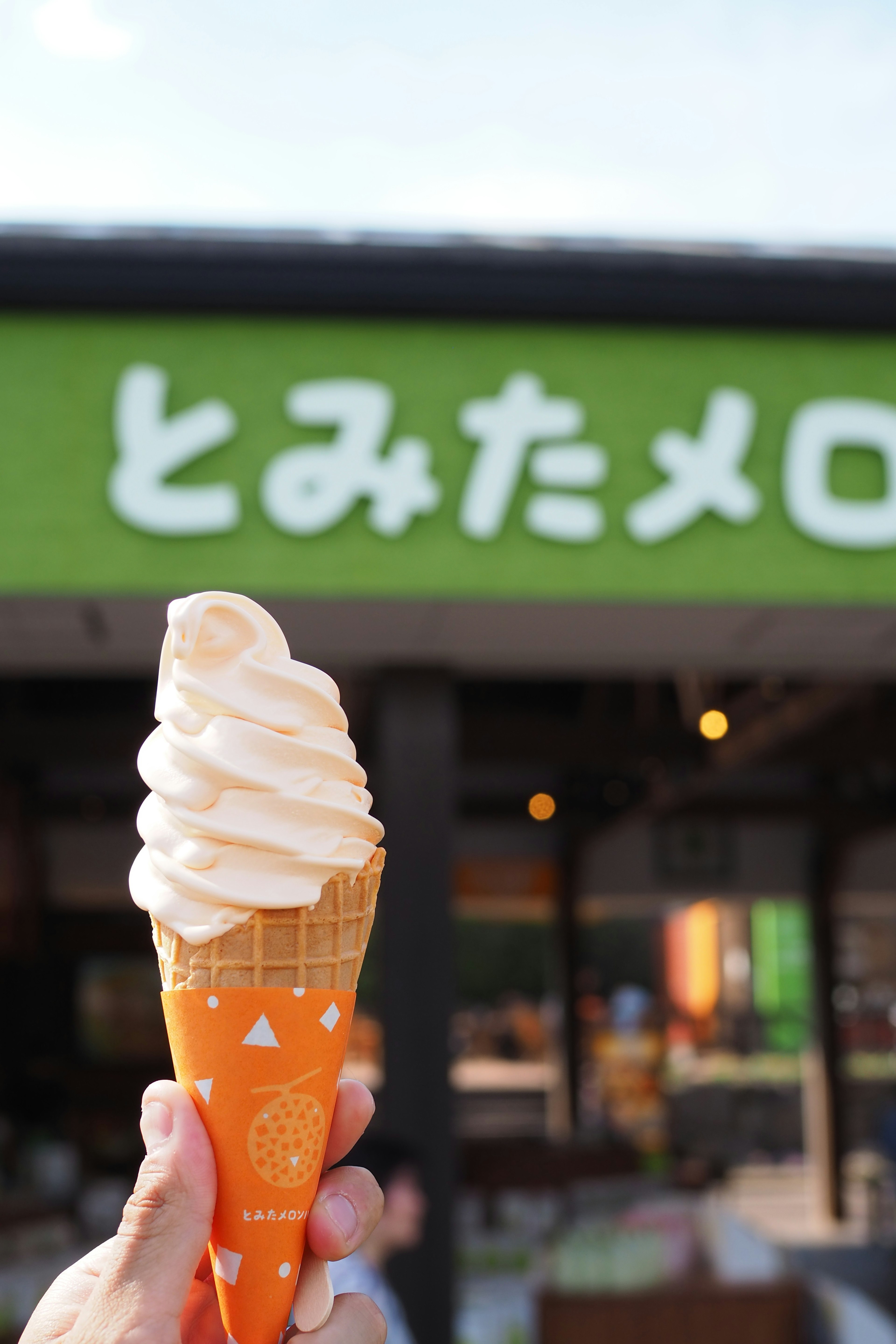 Mano sosteniendo un helado suave en un cono naranja con un letrero verde