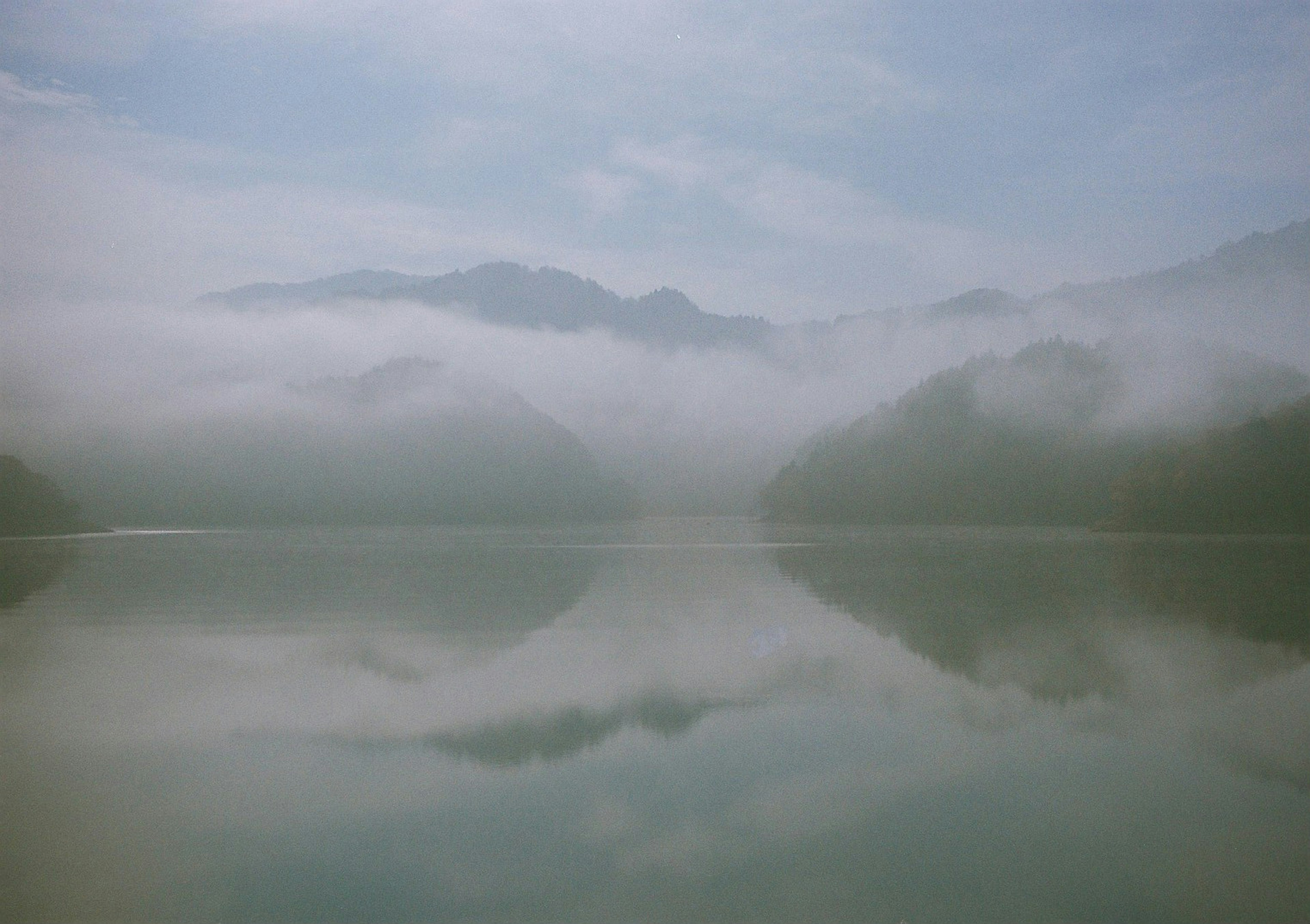 Un lago sereno rodeado de montañas brumosas reflejándose en el agua