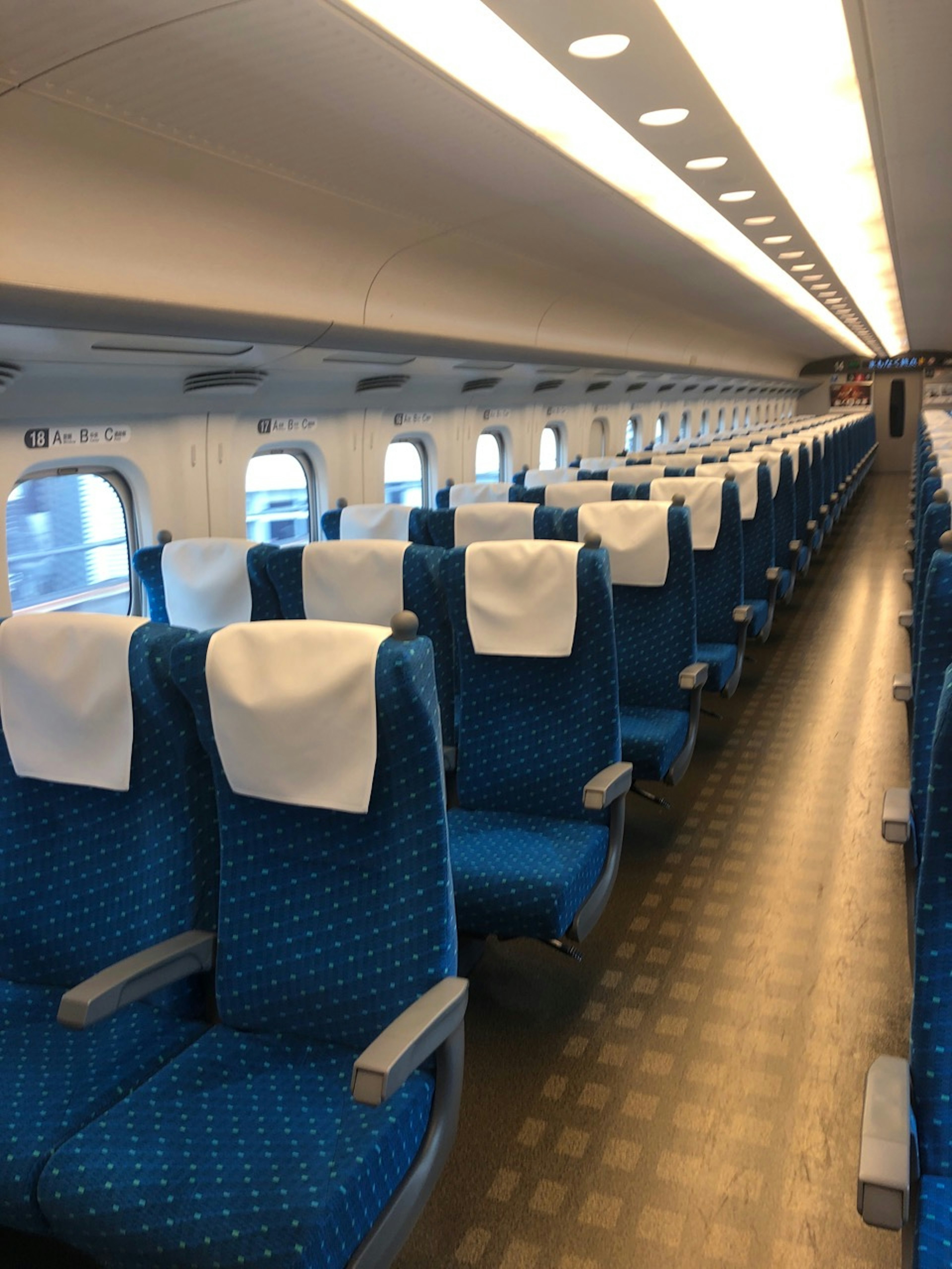 Interior of a Shinkansen train featuring blue seats with white headrest covers