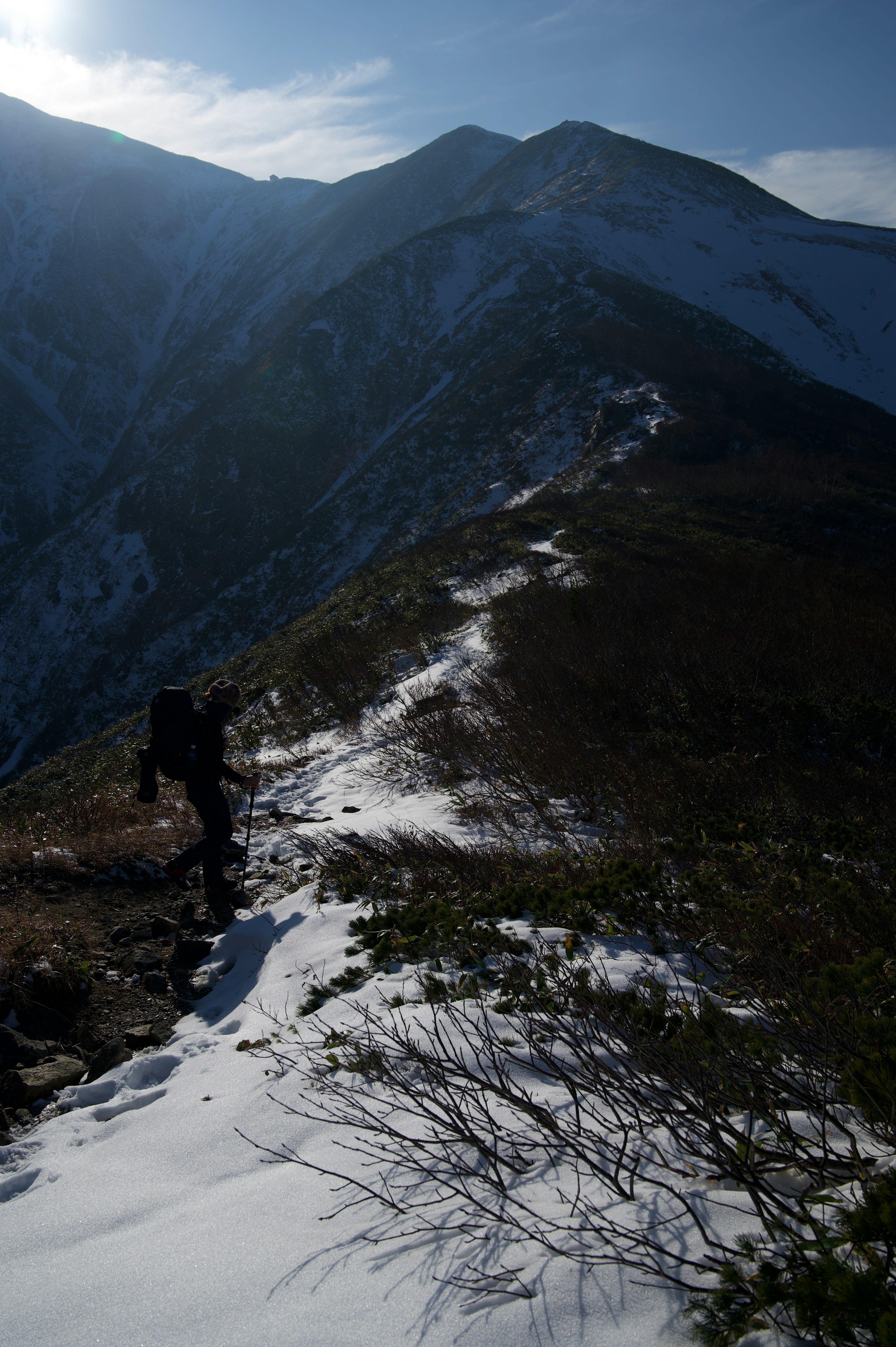 雪のある山道を歩くハイカーのシルエットと険しい山々