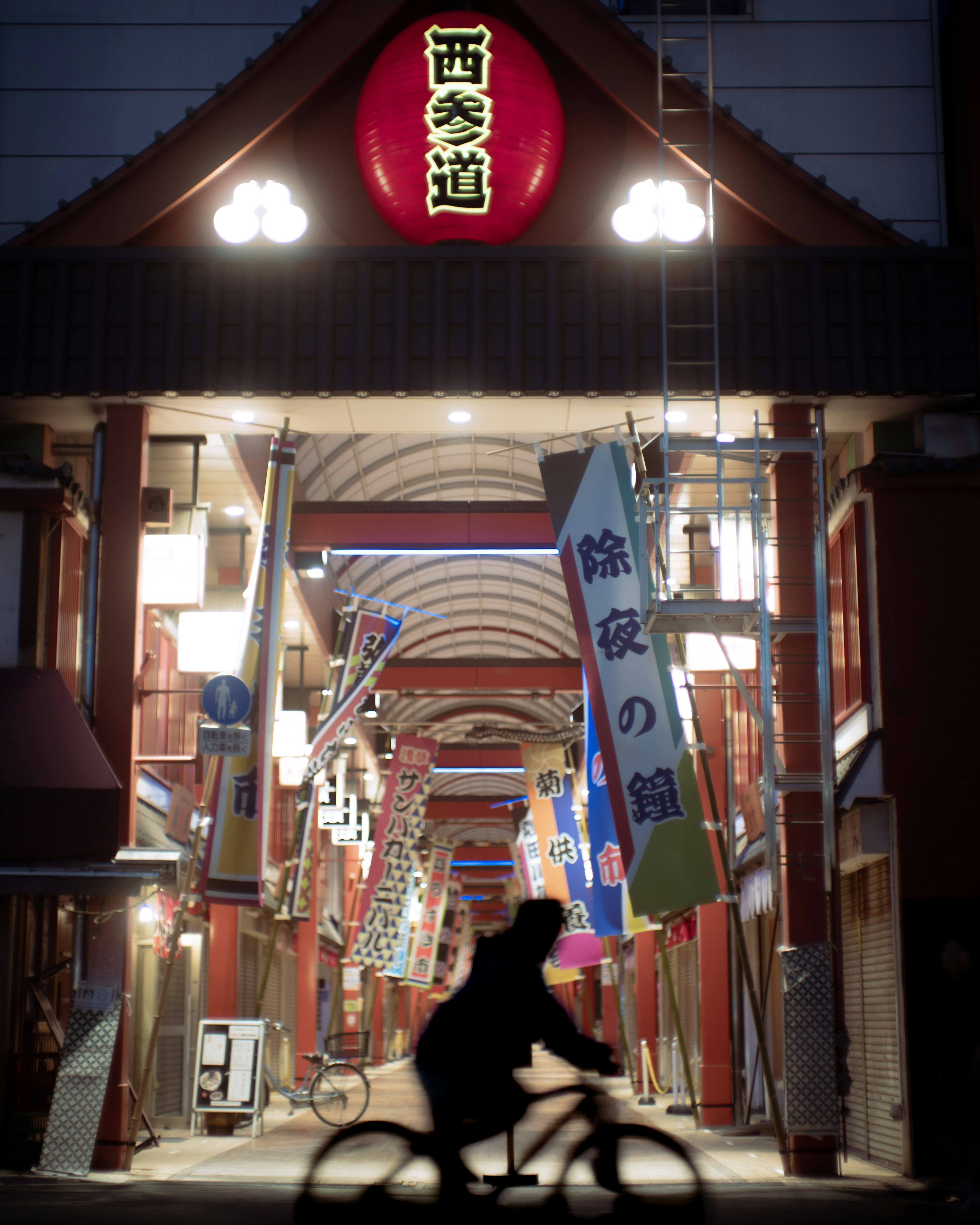 Silhouette of a person cycling in a night shopping street with lantern lights