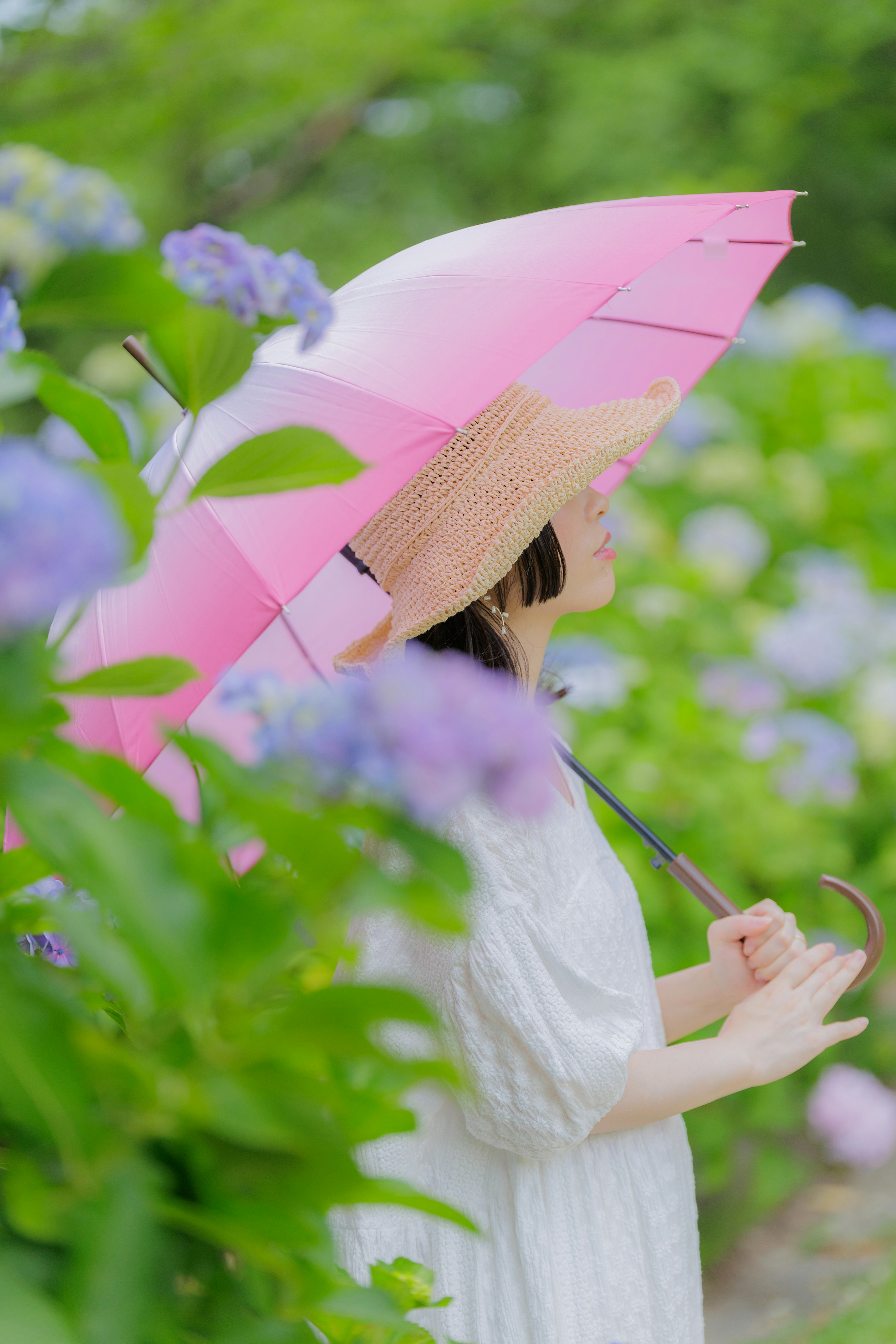 Eine Frau in einem weißen Kleid, die einen rosa Regenschirm hält, umgeben von Hortensienblüten