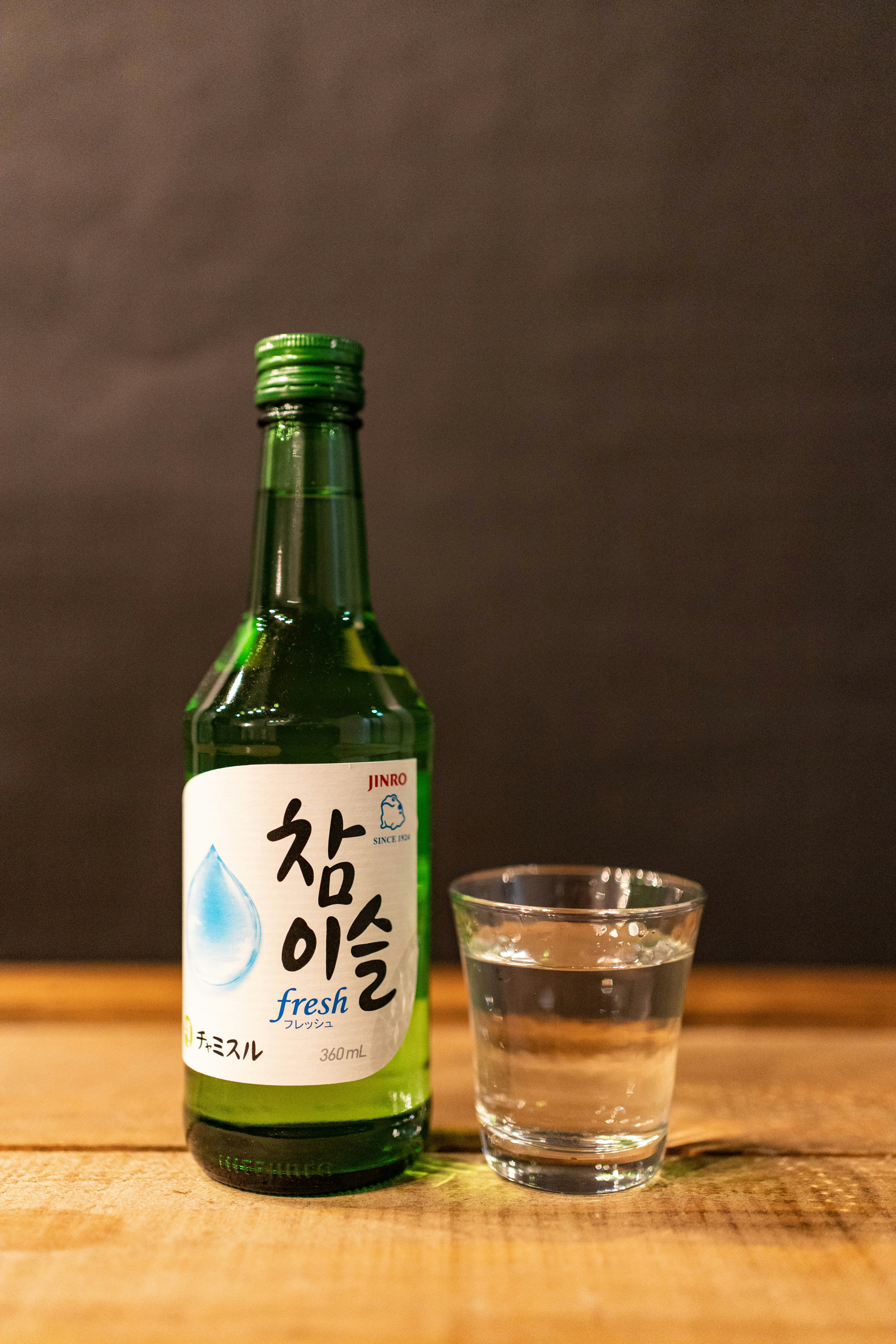 緑色の瓶に入った韓国の焼酎と透明なグラスが木のテーブルに置かれている