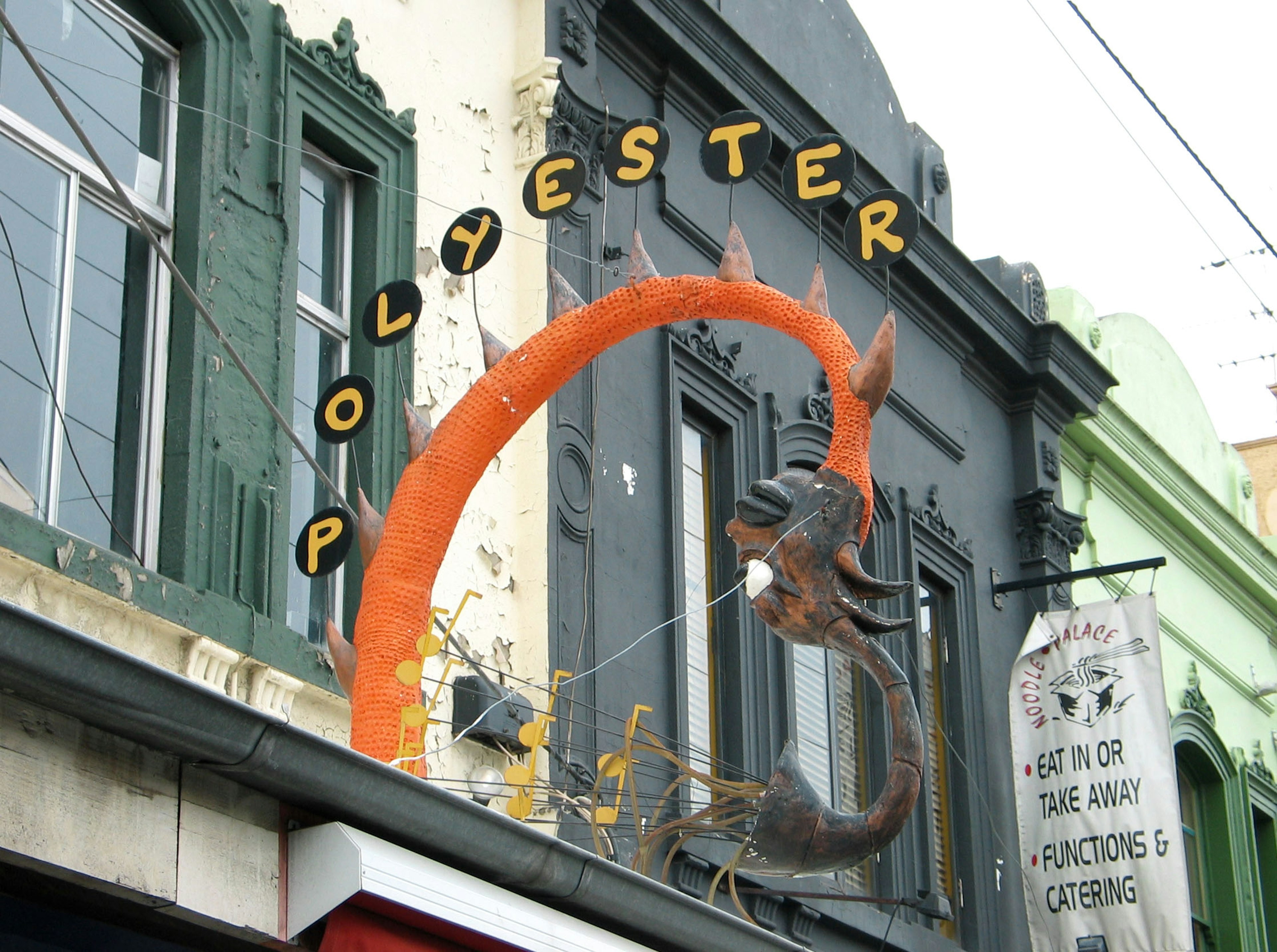 Colorful sign with dragon sculpture above Polyester store