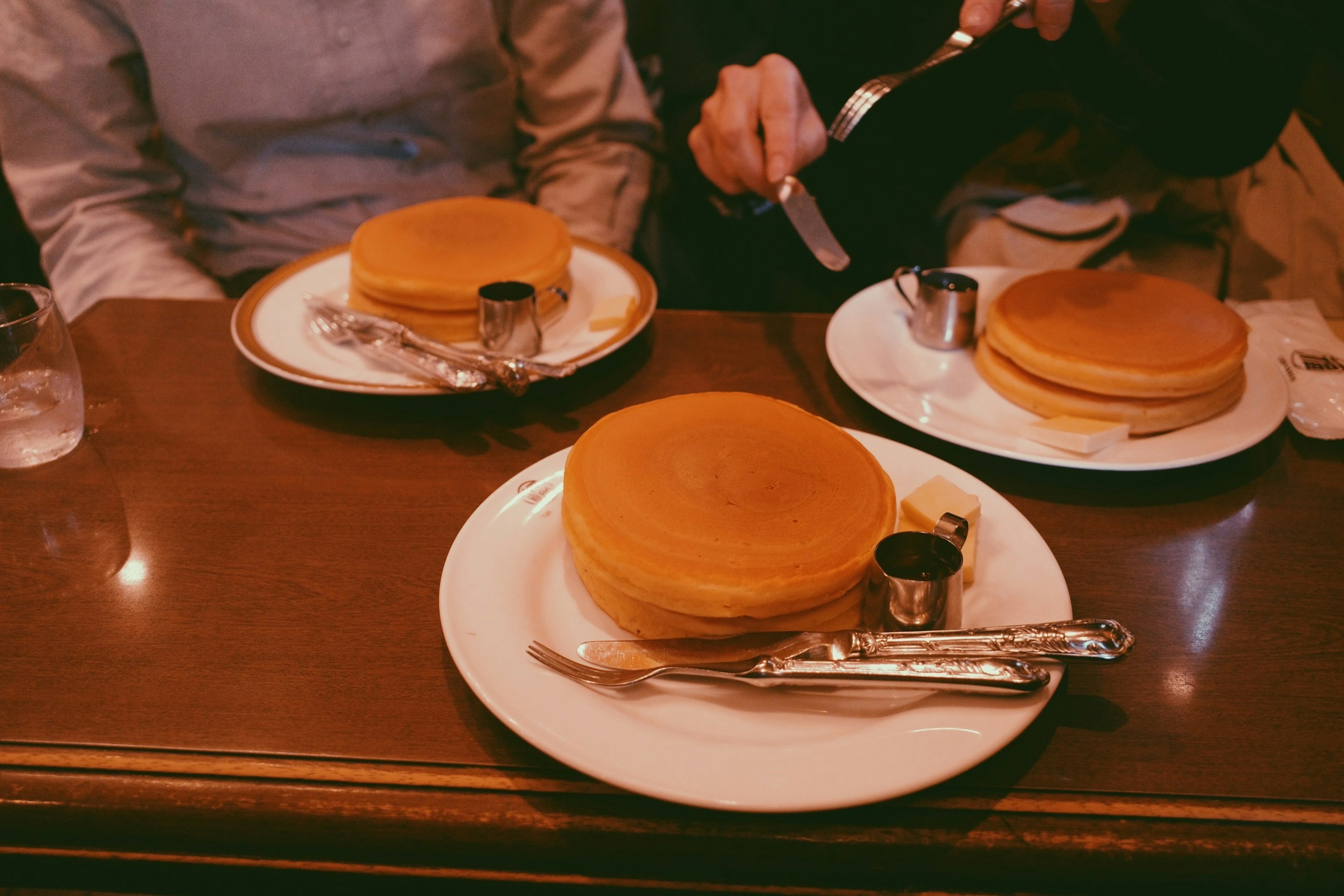 Gestapelte Pfannkuchen auf weißen Tellern mit Sirup und Besteck