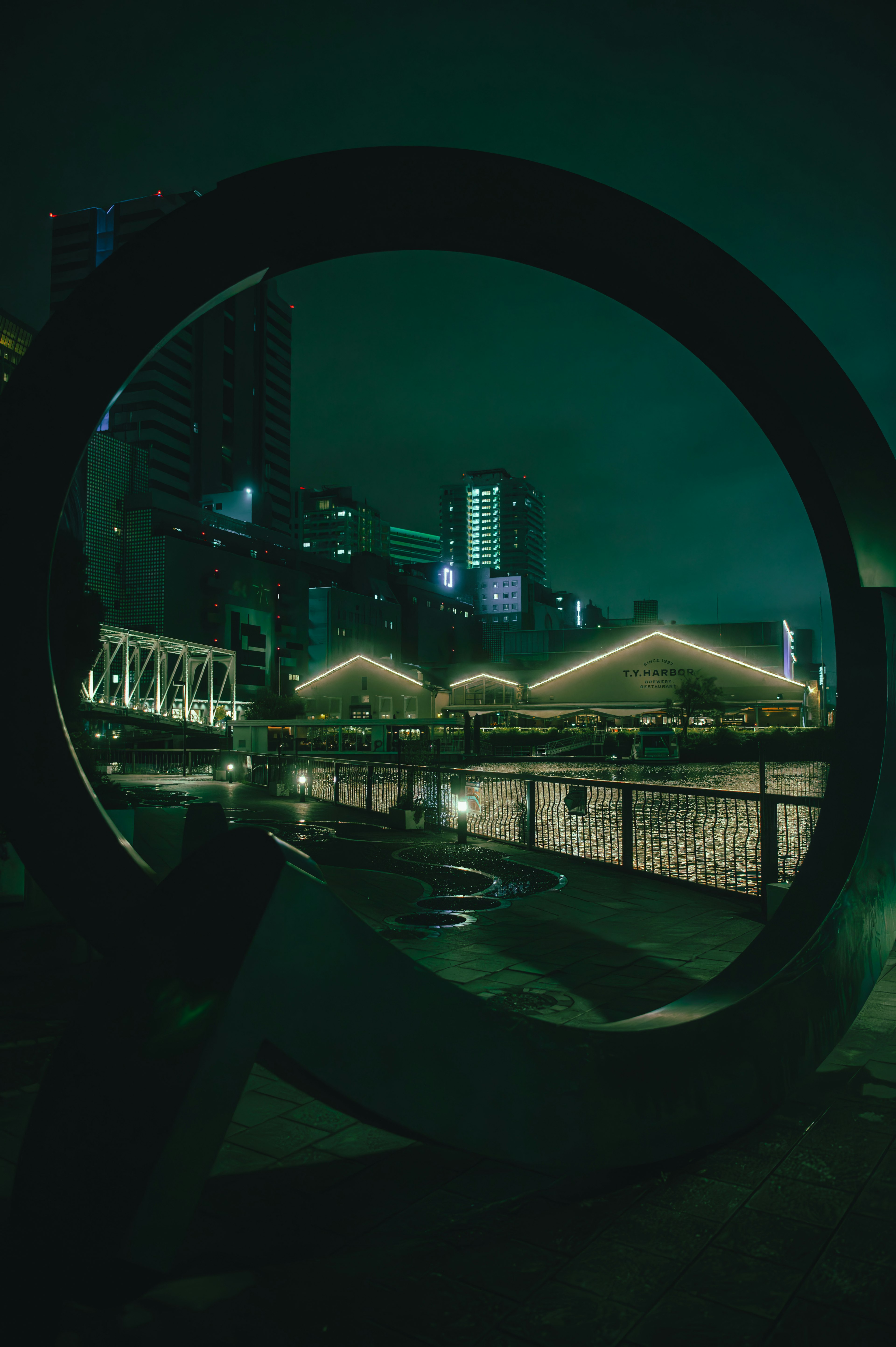 Urban night scene framed by a circular structure Bright buildings and green lighting are striking