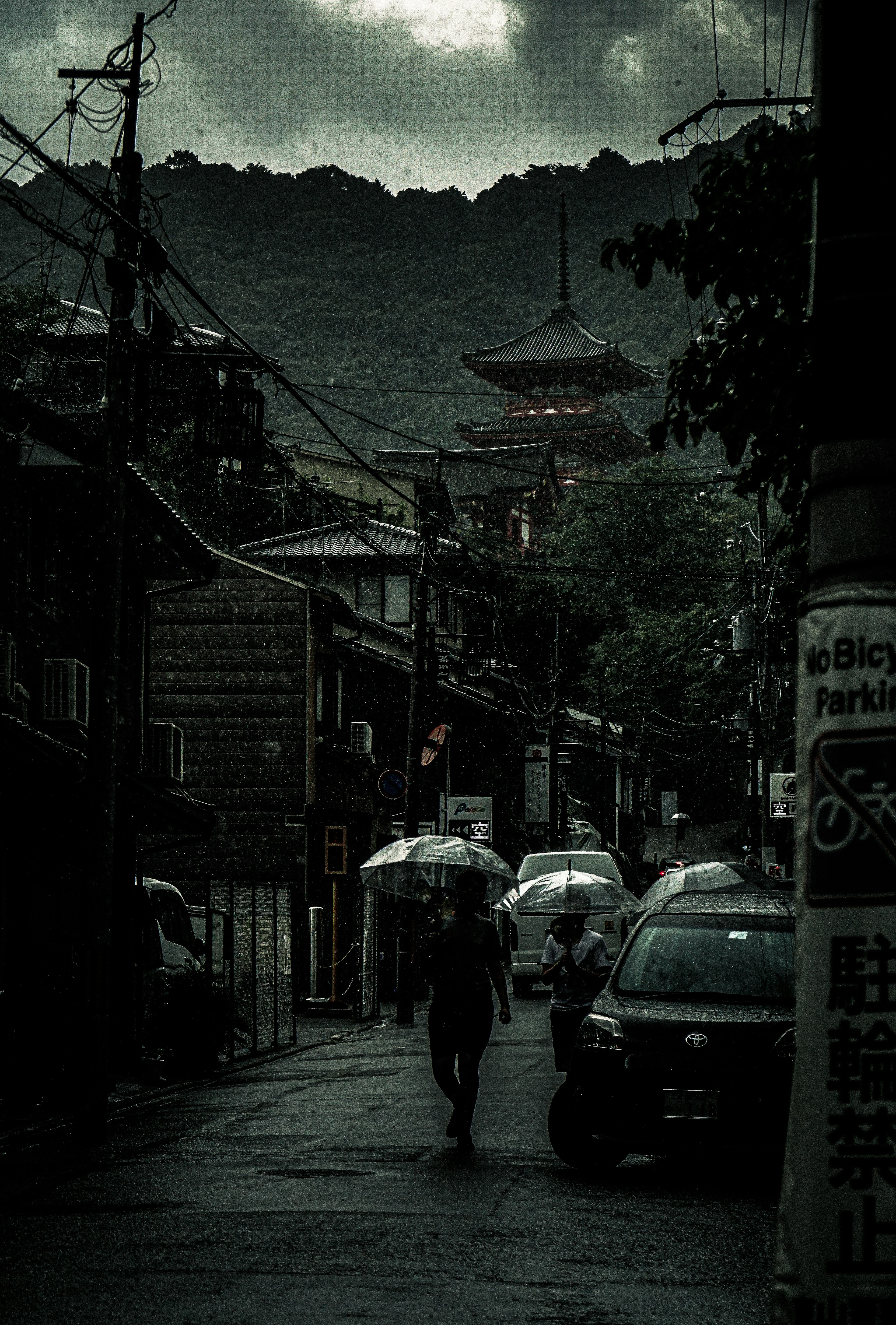 暗い雲の下の街並みと傘を持った人が歩く風景