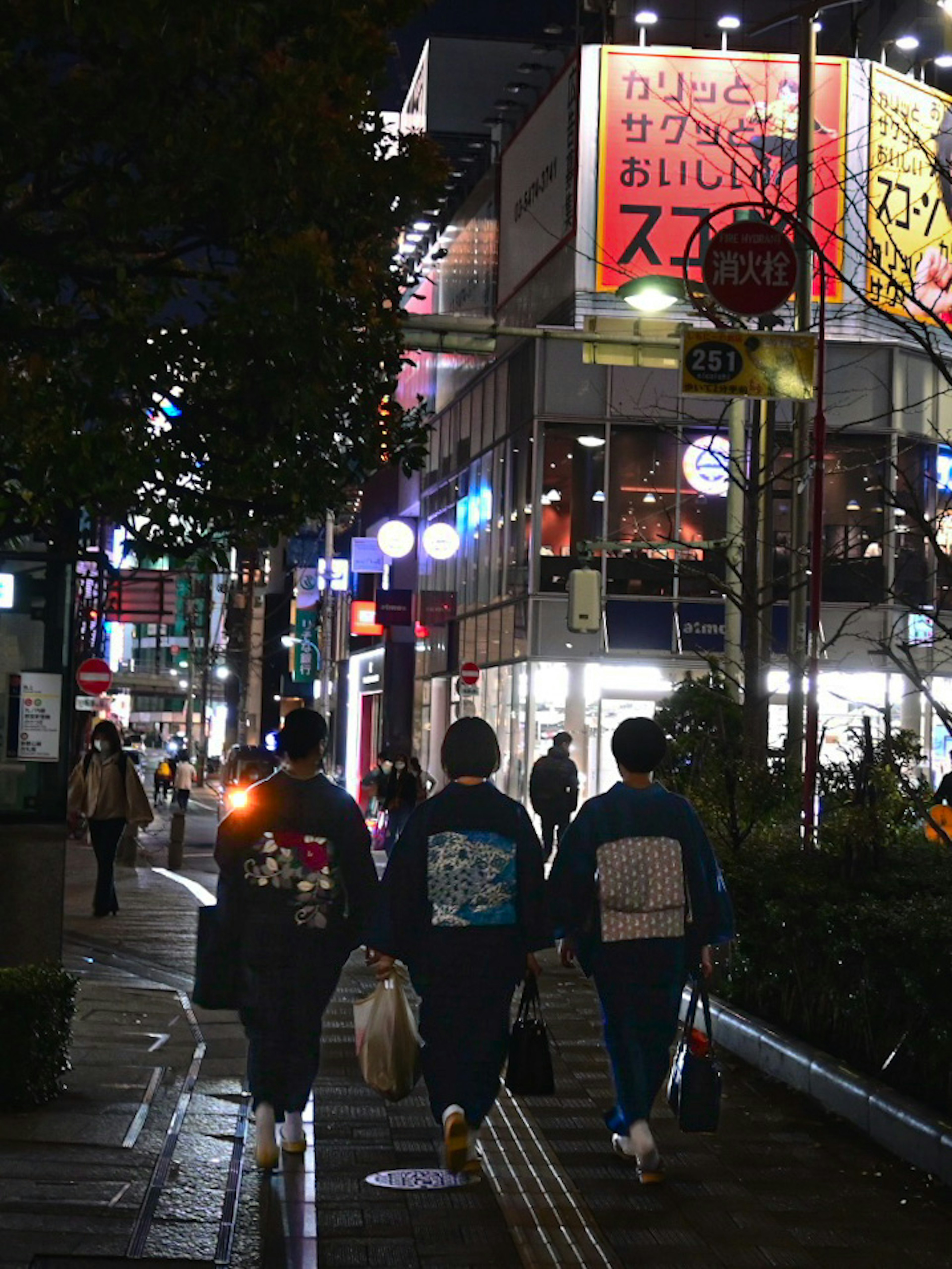 Tres personas caminando en la calle de noche con letreros brillantes