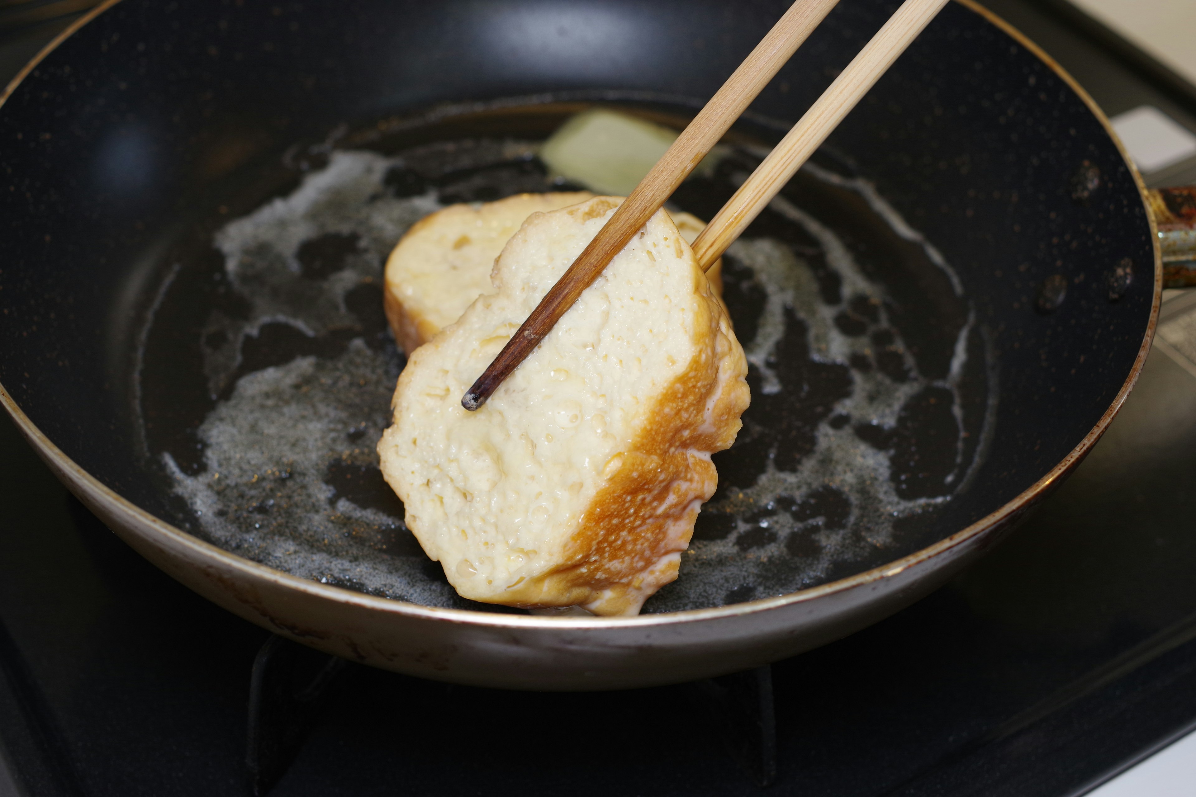 Toast being flipped in a frying pan with chopsticks