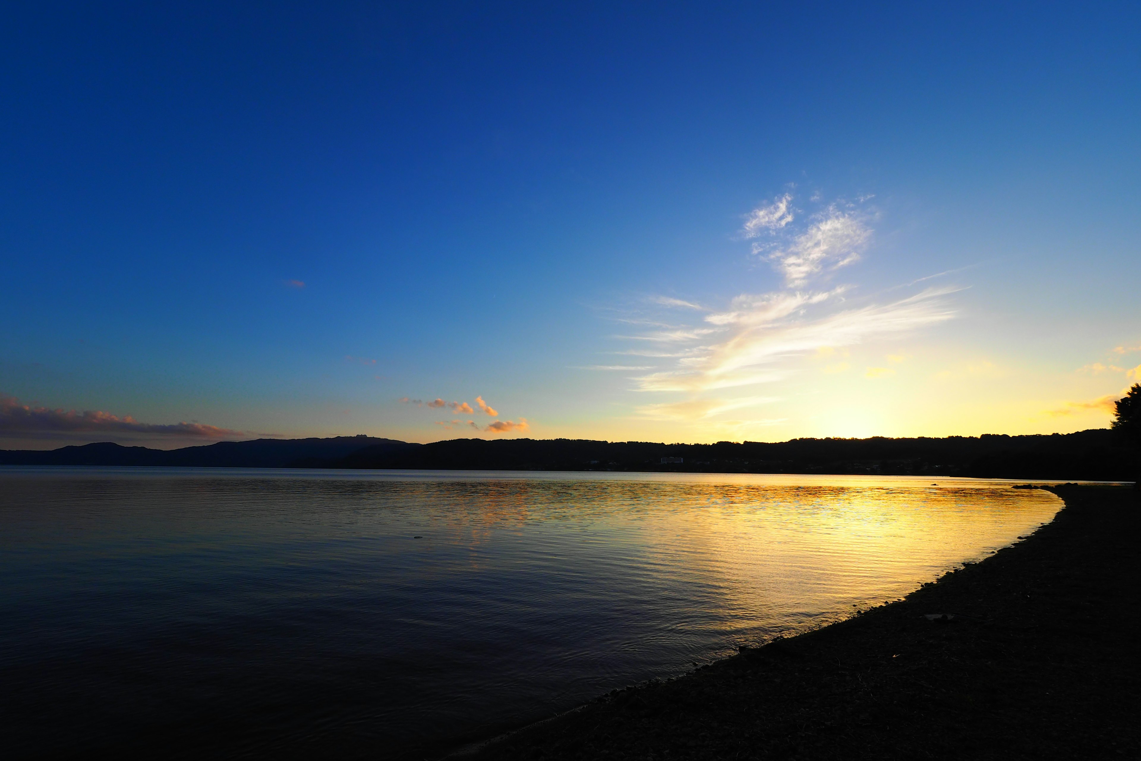 Ruhiger Sonnenuntergang am See mit blauem Himmel und goldenem Reflex