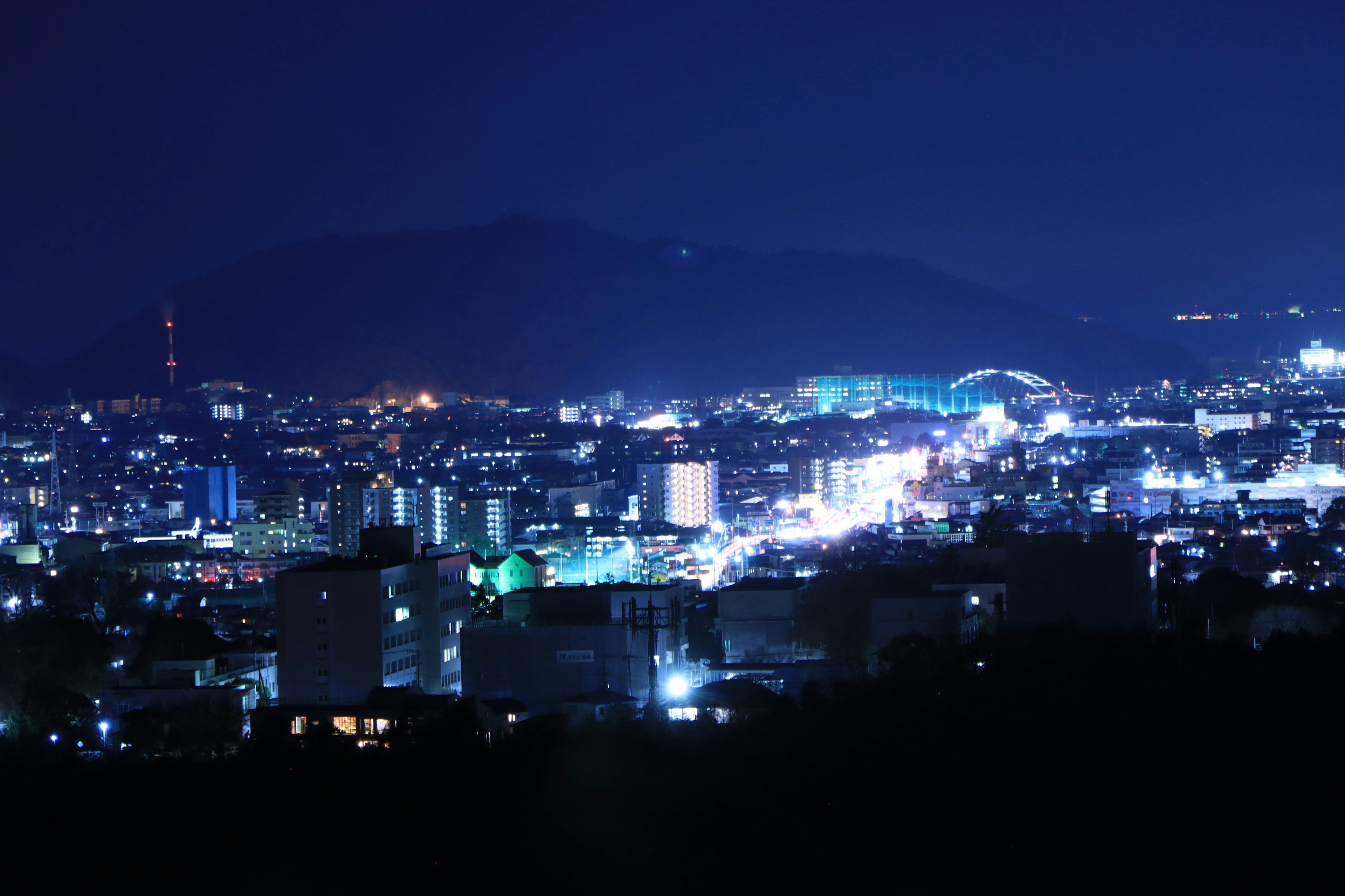 Vista nocturna de un paisaje urbano con edificios iluminados en azul y montañas de fondo