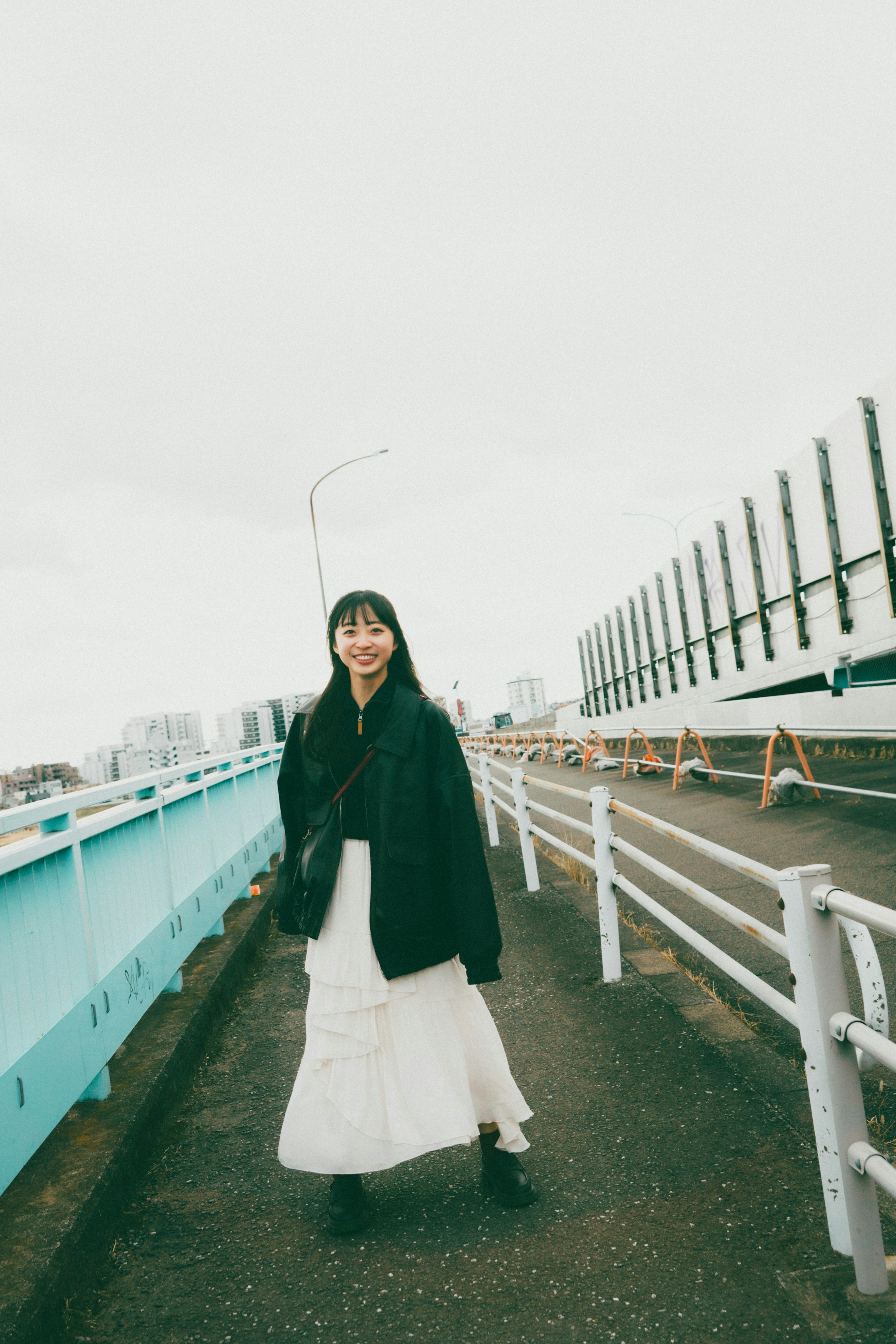 A woman in a white skirt and black coat standing on a street with a cloudy sky