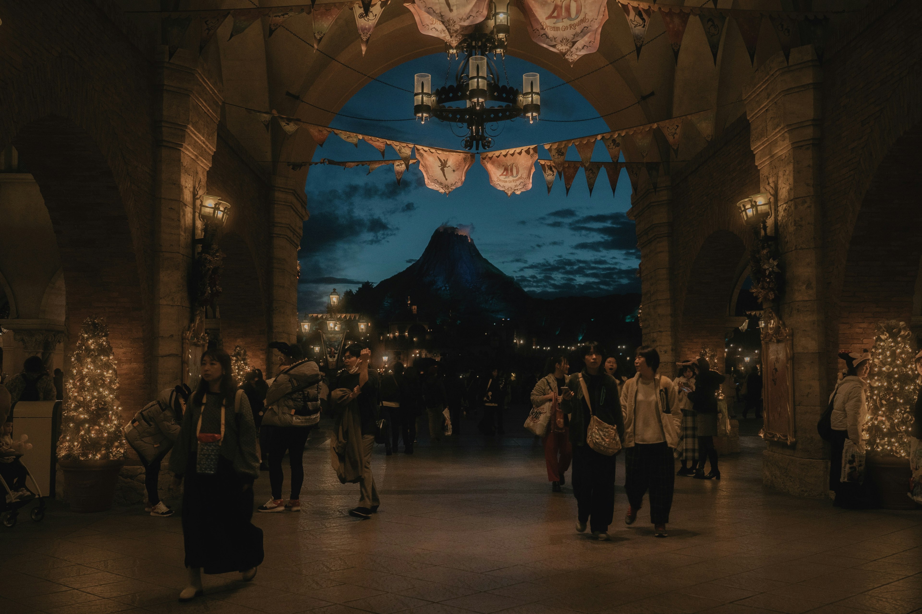 Vista de entrada con personas caminando bajo arcos decorados con luces y una montaña al fondo