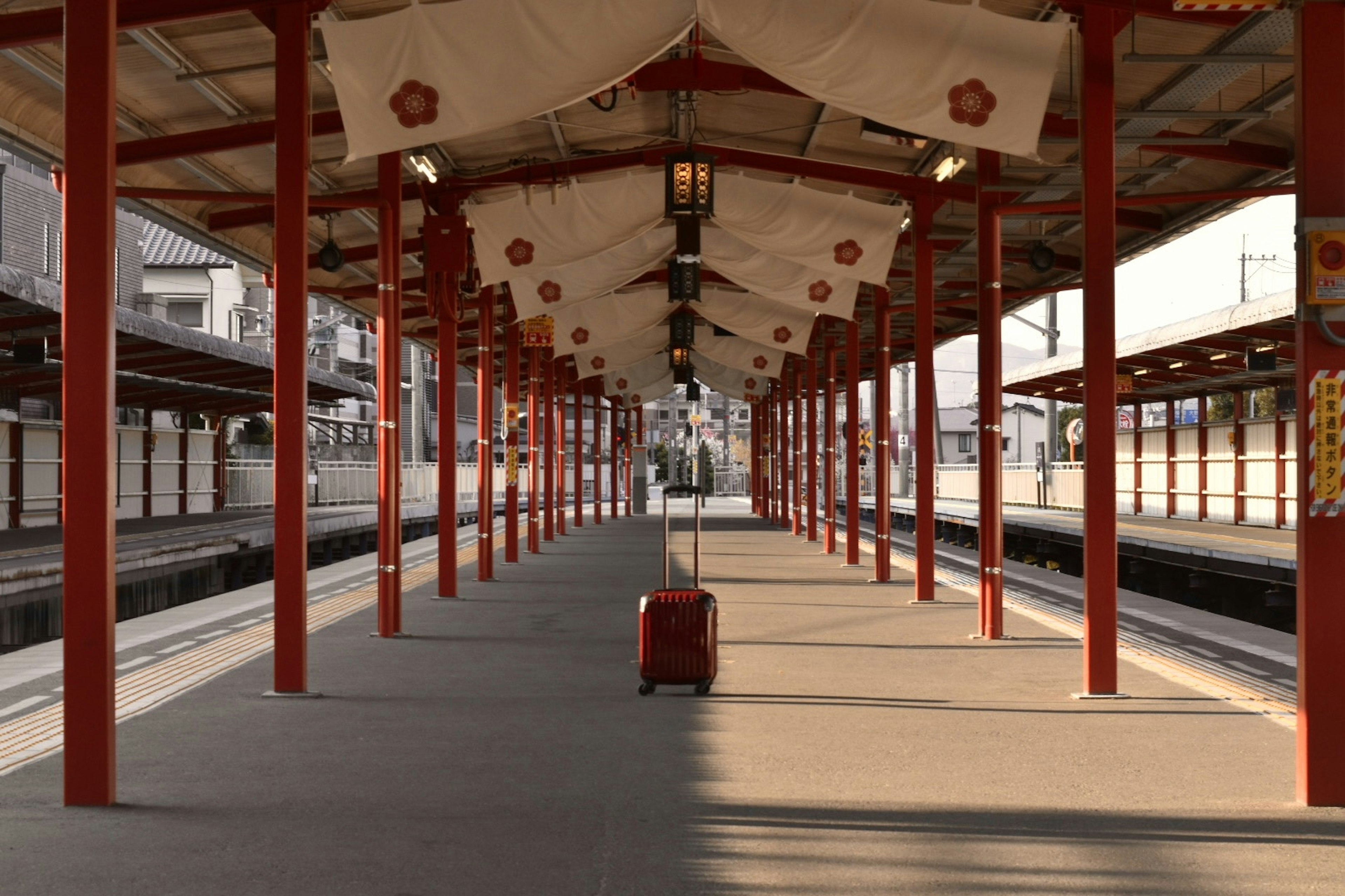 Train station platform featuring red pillars and a suitcase