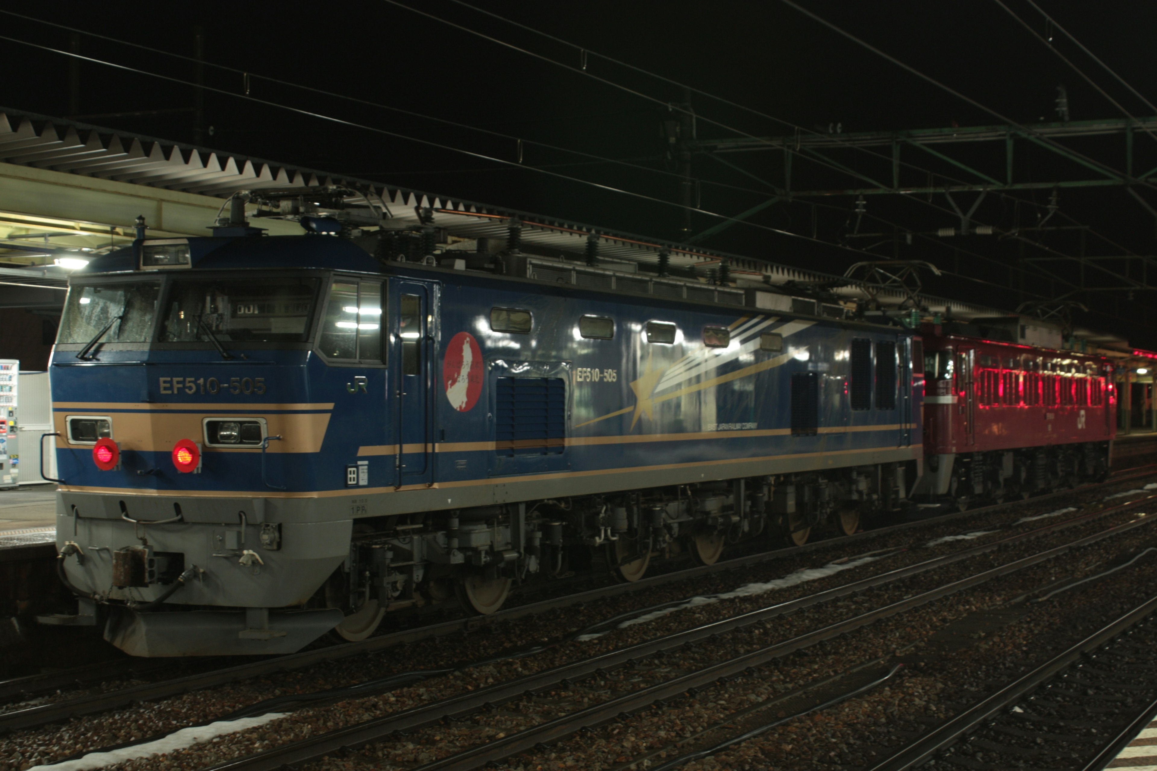 Blue electric locomotive and red freight train at night in a station