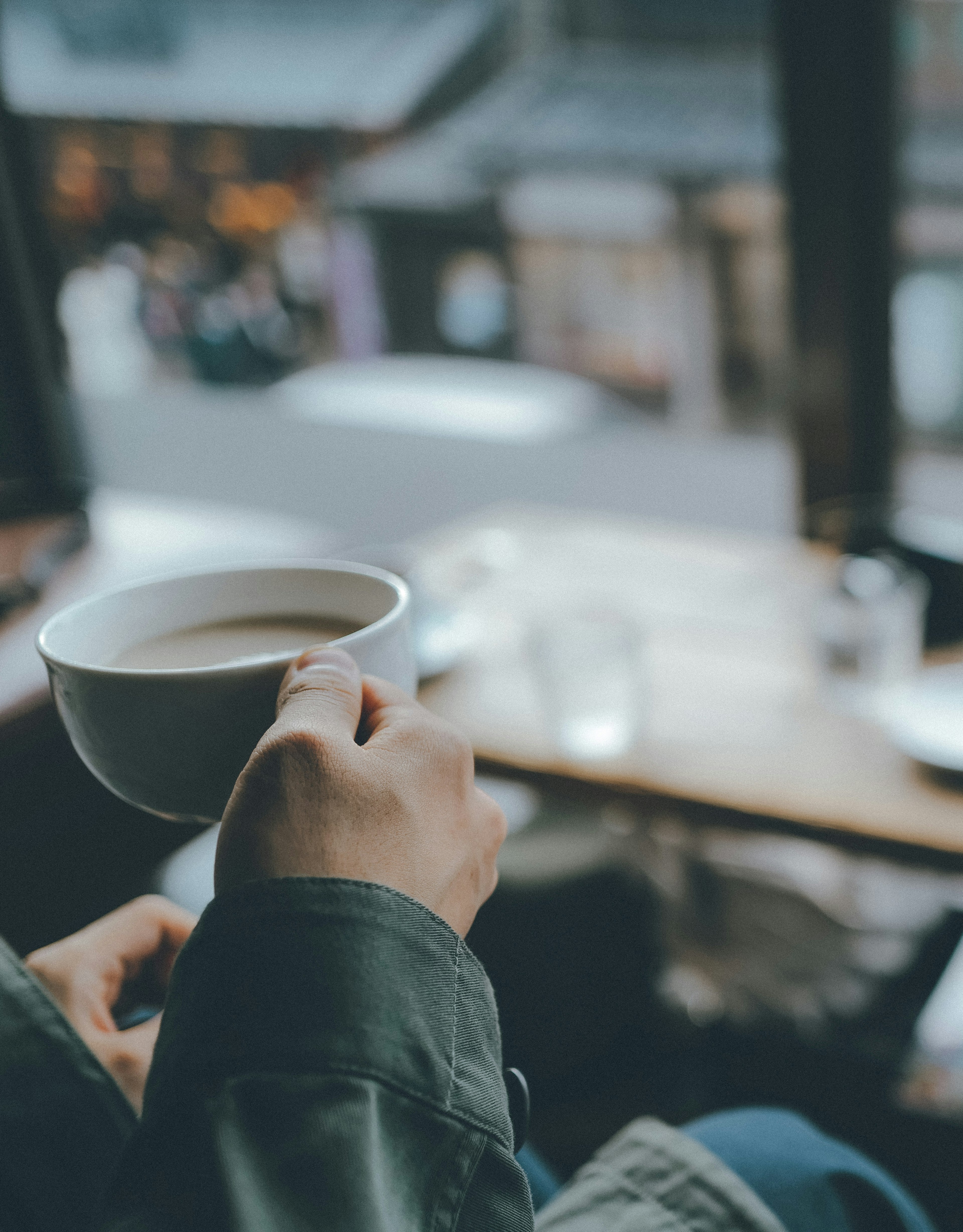 Primer plano de una mano sosteniendo una taza de café en una cafetería con un fondo borroso afuera