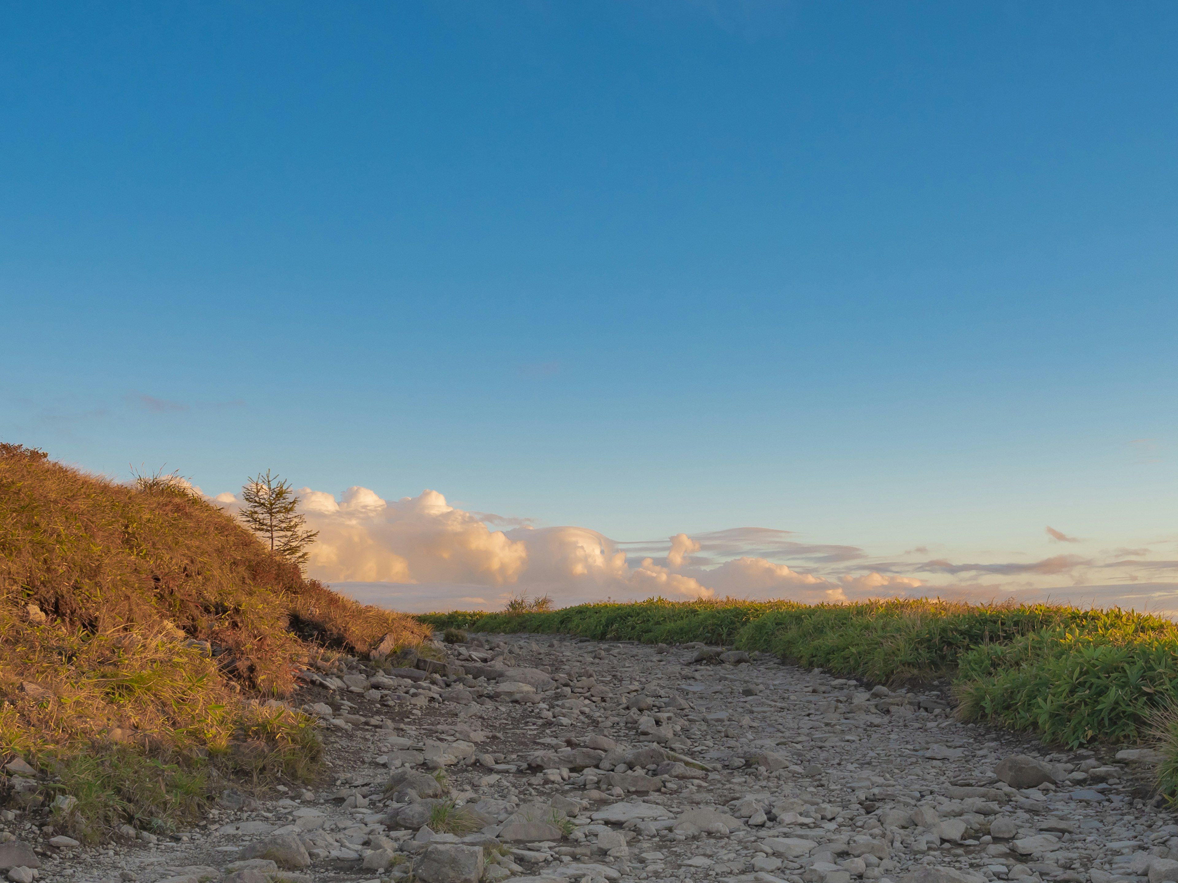 Un chemin rocailleux menant à un paysage avec ciel bleu et nuages