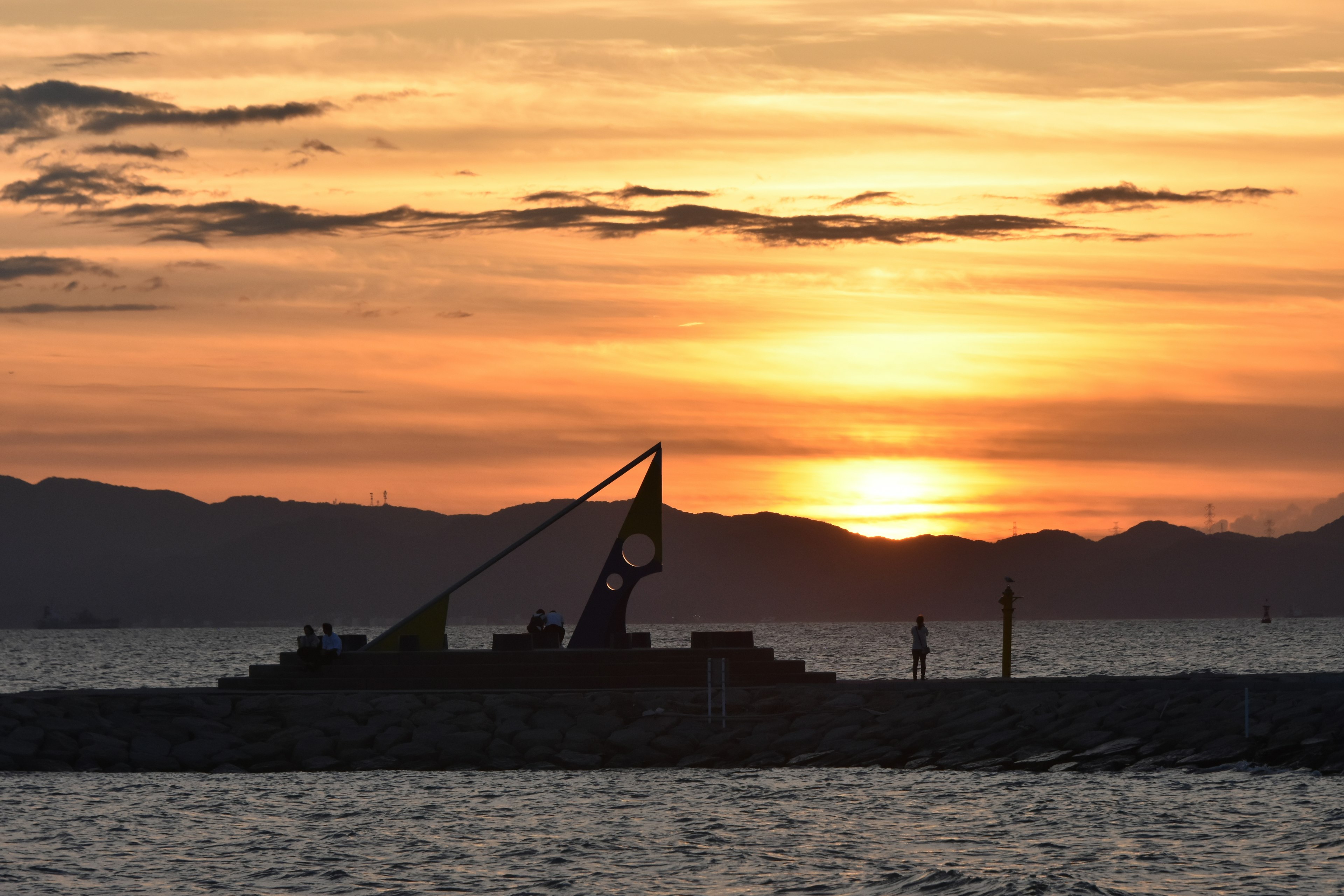 夕日を背景にした海岸のシルエットにある大きな時計のある構造物