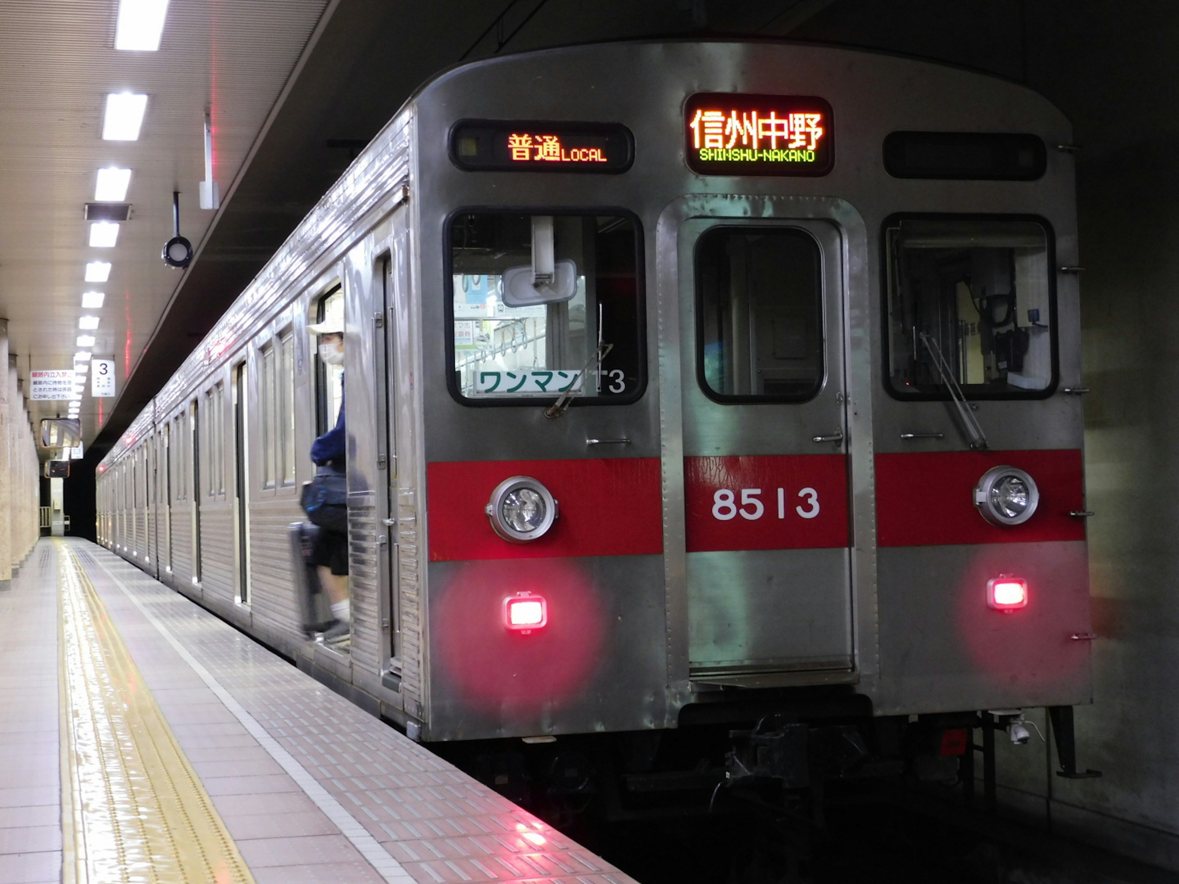 Tren de metro plateado con franjas rojas parado en la estación