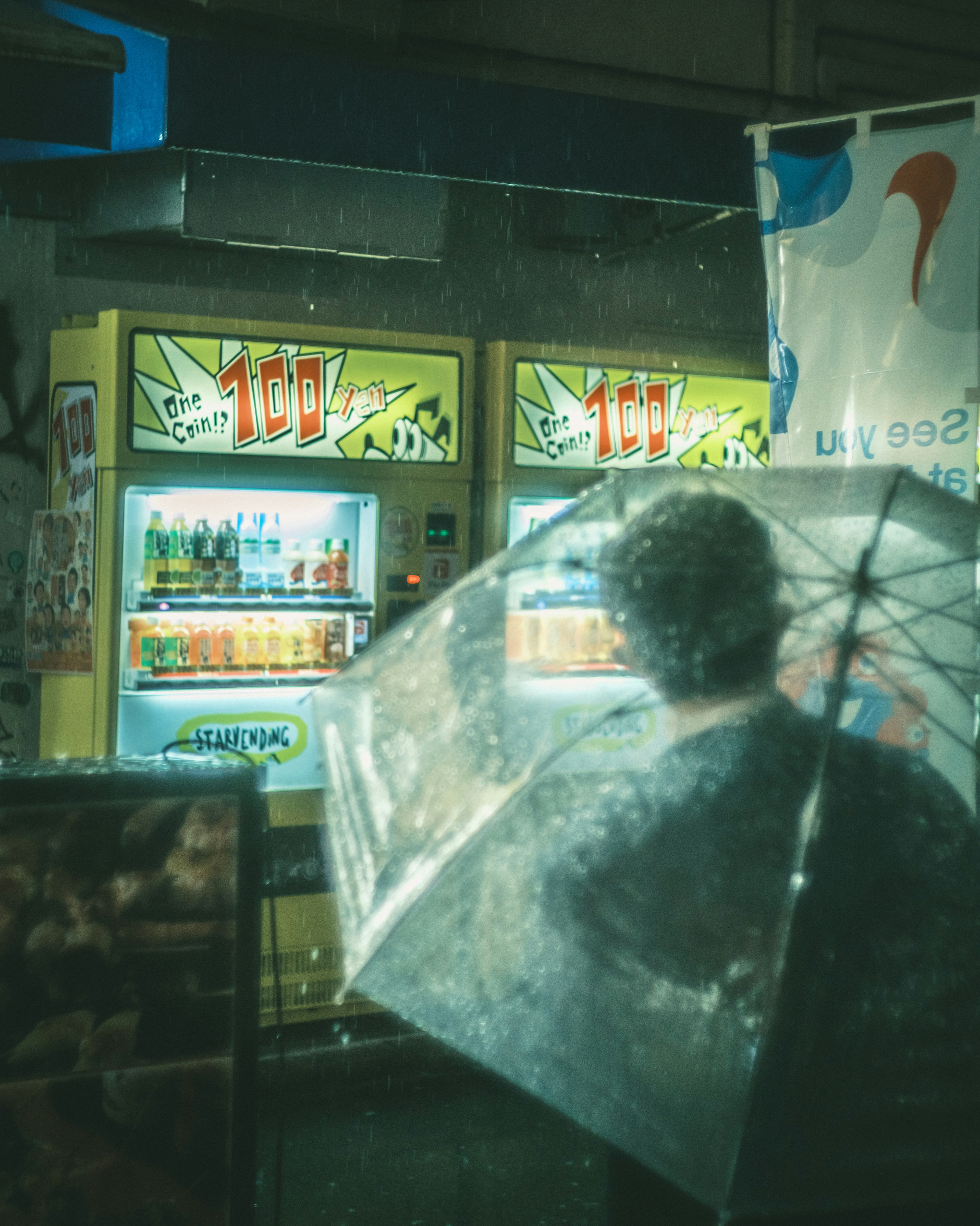 Personne tenant un parapluie transparent devant des distributeurs automatiques par un jour de pluie