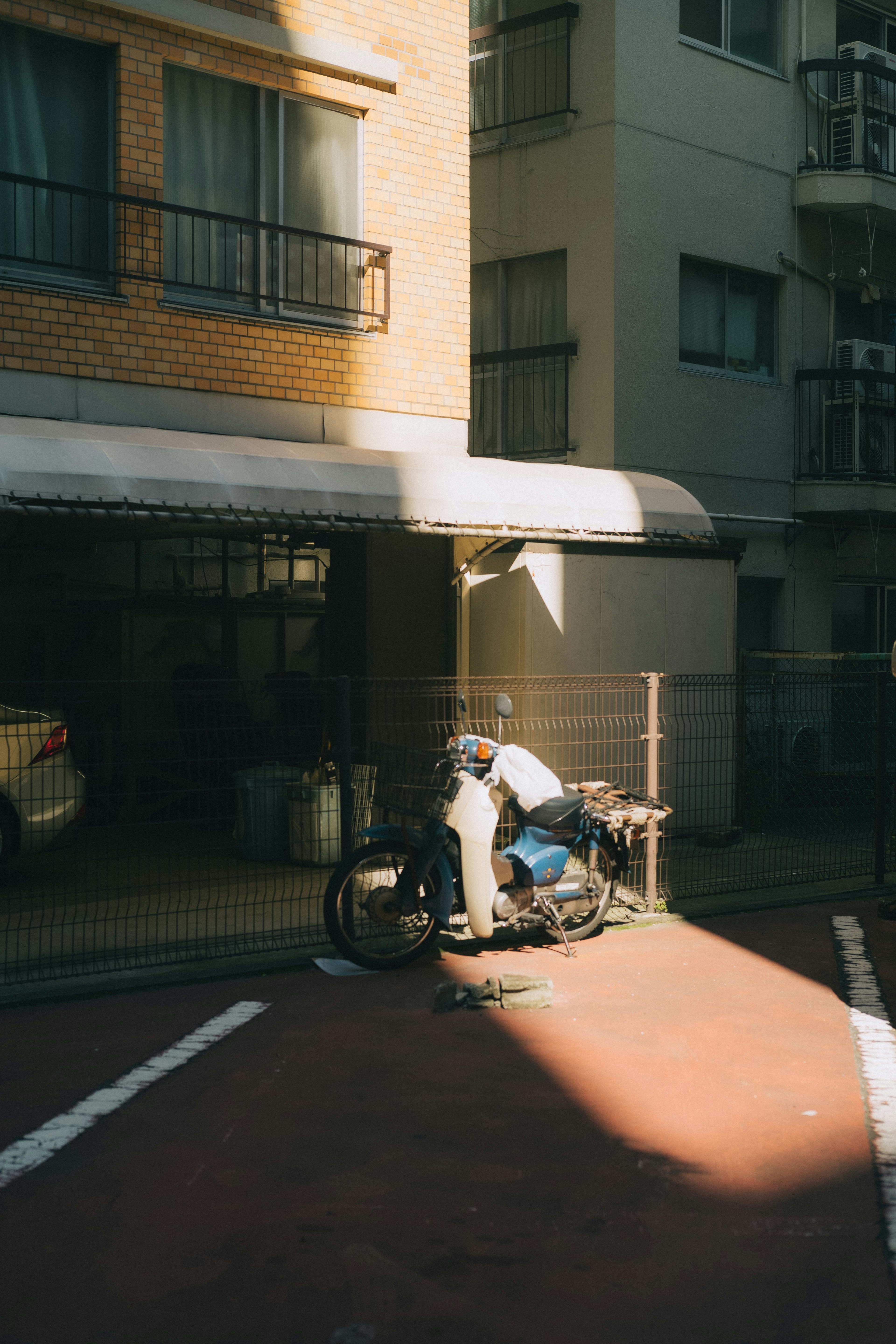 Person sitting on a motorcycle in sunlight near an apartment