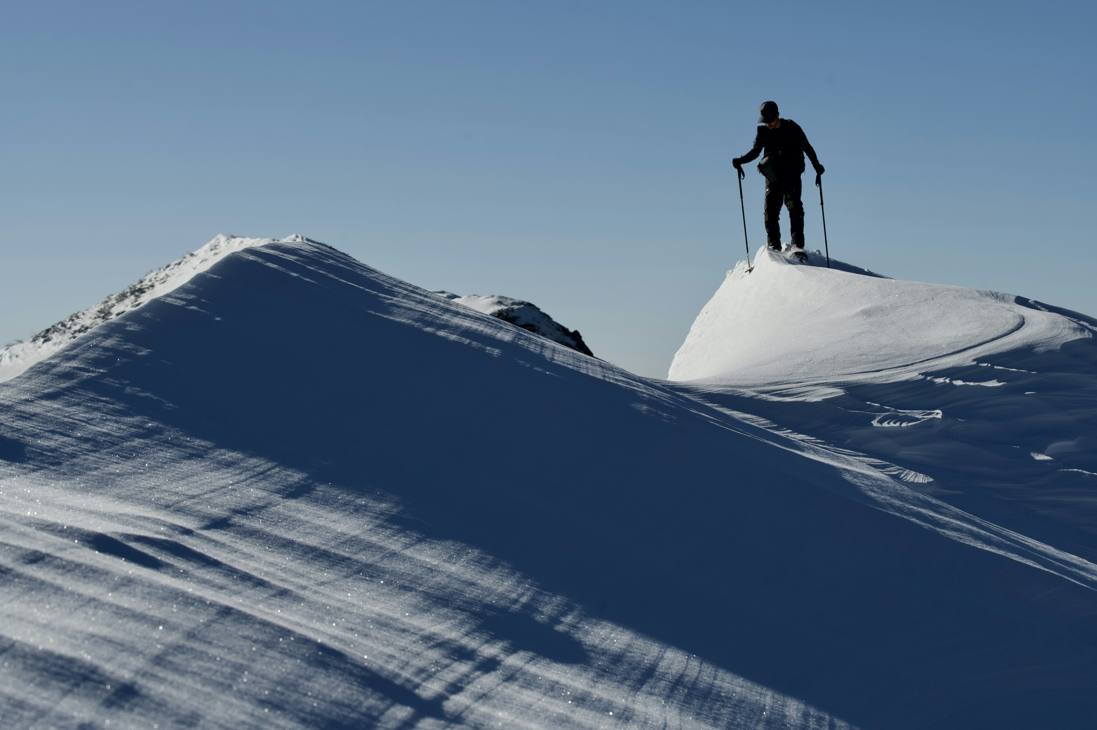 Person standing on a snow-covered mountain peak holding ski poles