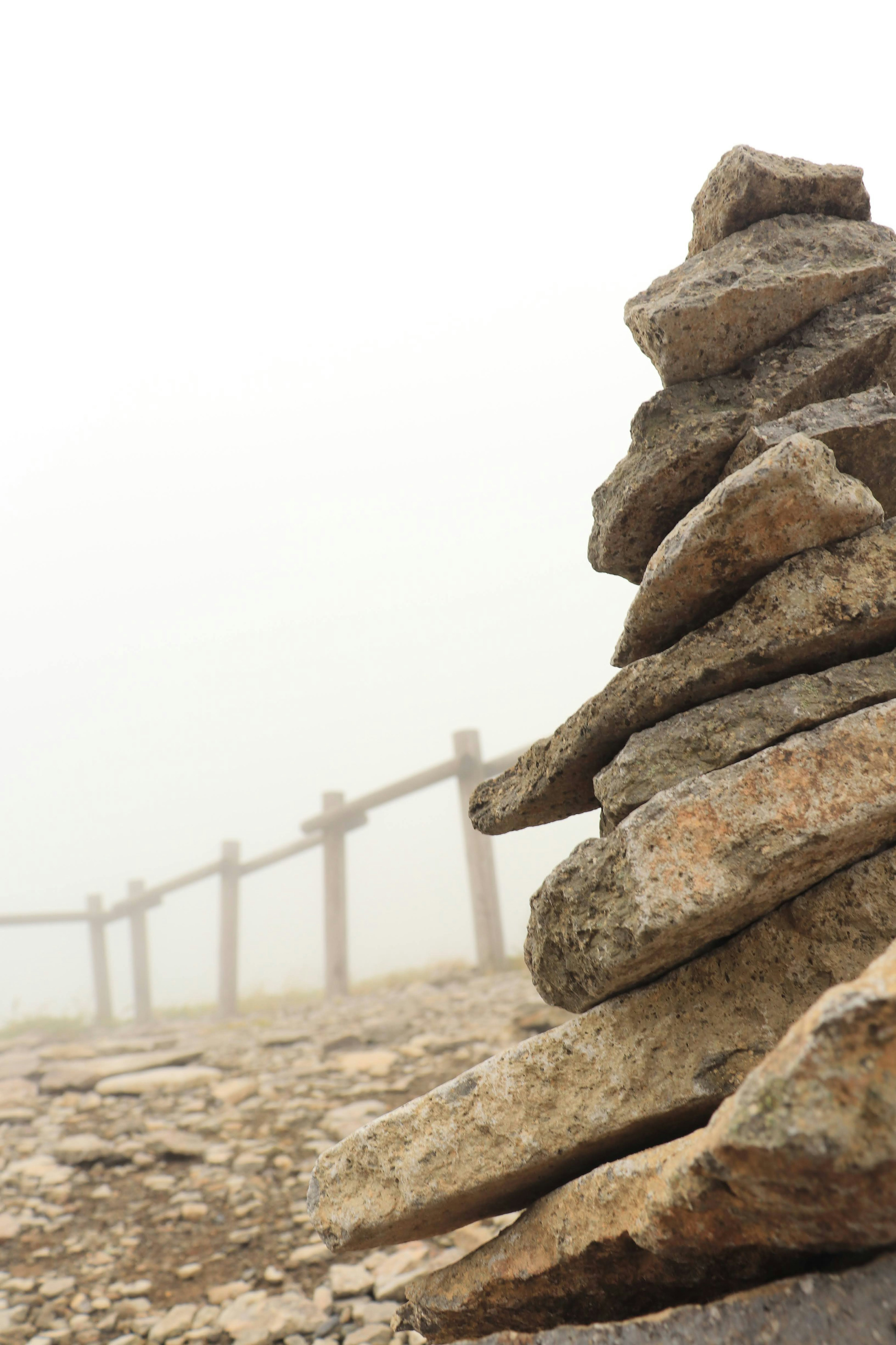 Pila de piedras en la niebla con una cerca de madera al fondo