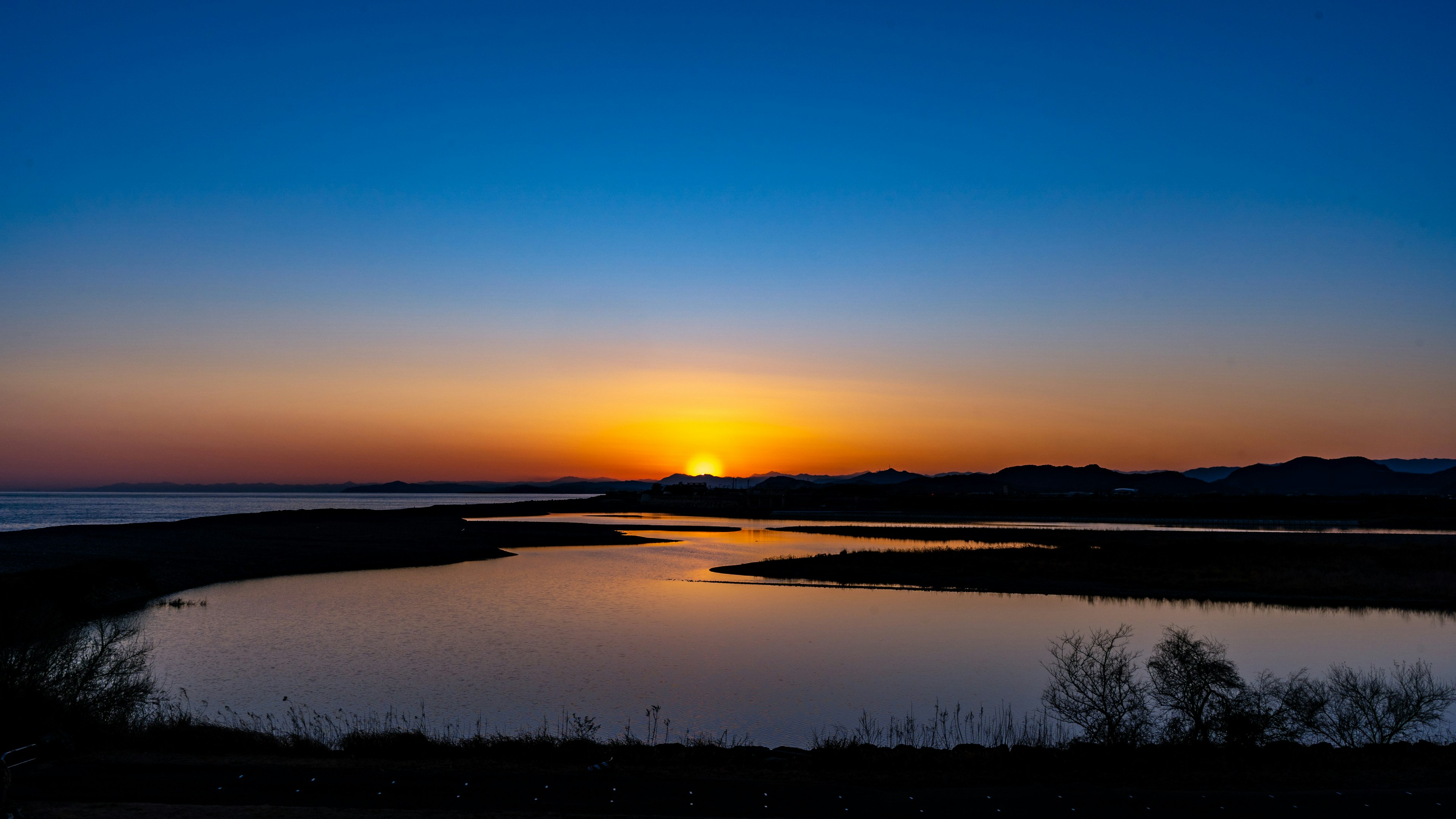 Sunset over calm waters with a blue sky