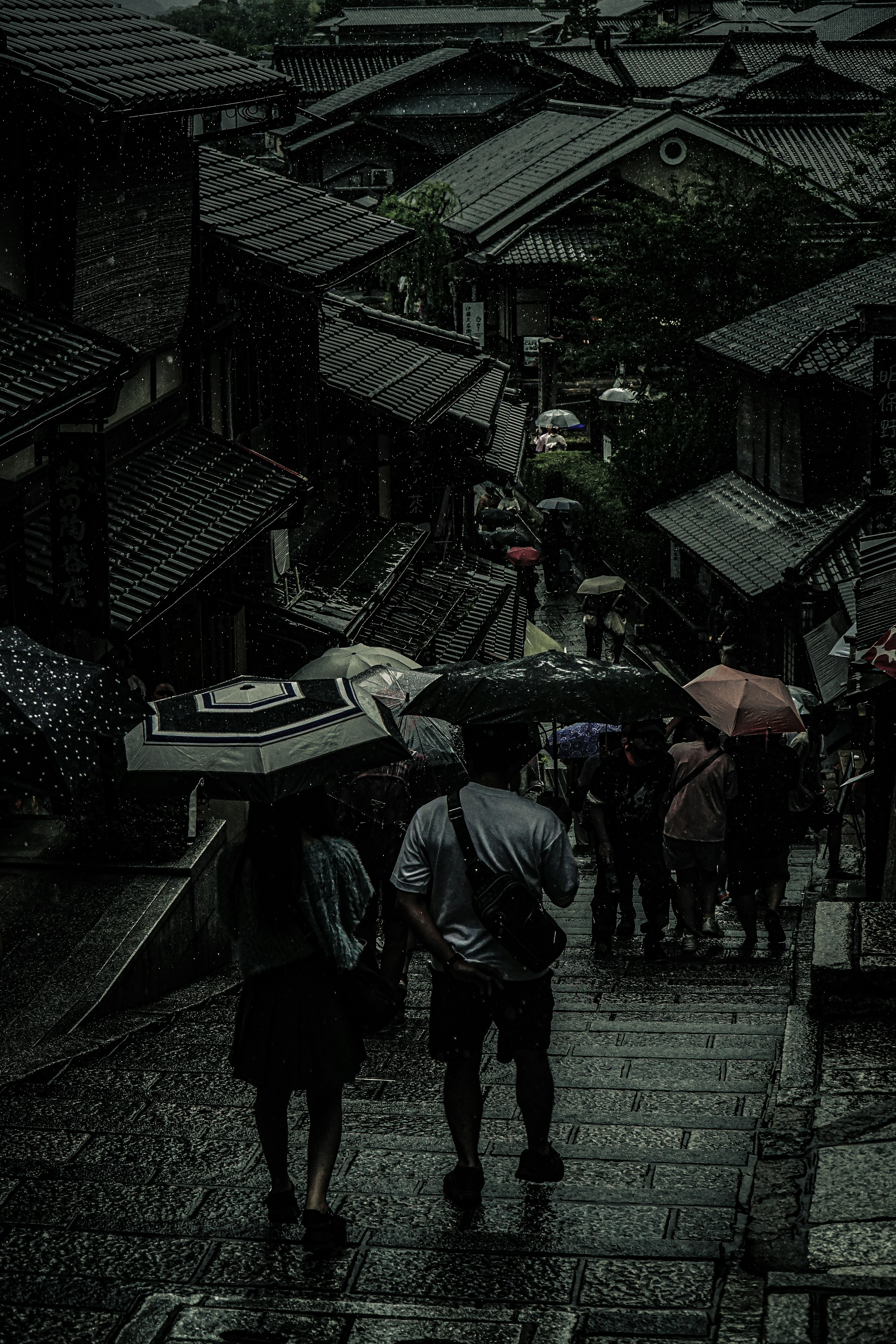 雨の中を傘を持って歩く人々の風景 石畳の階段と古い家屋が並ぶ街並み