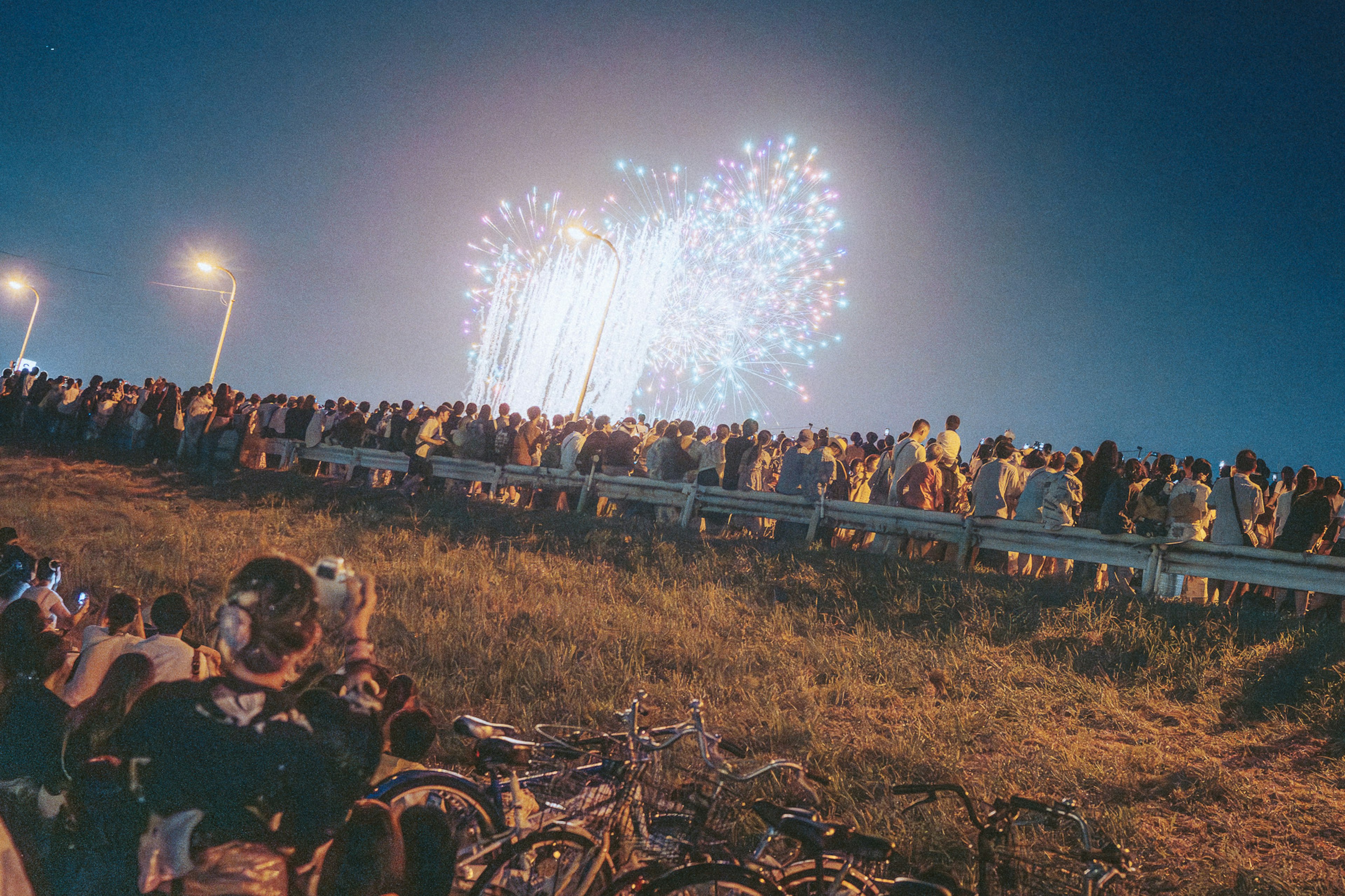 Menschenmenge, die ein Feuerwerk bei Nacht betrachtet, mit Fahrrädern im Vordergrund