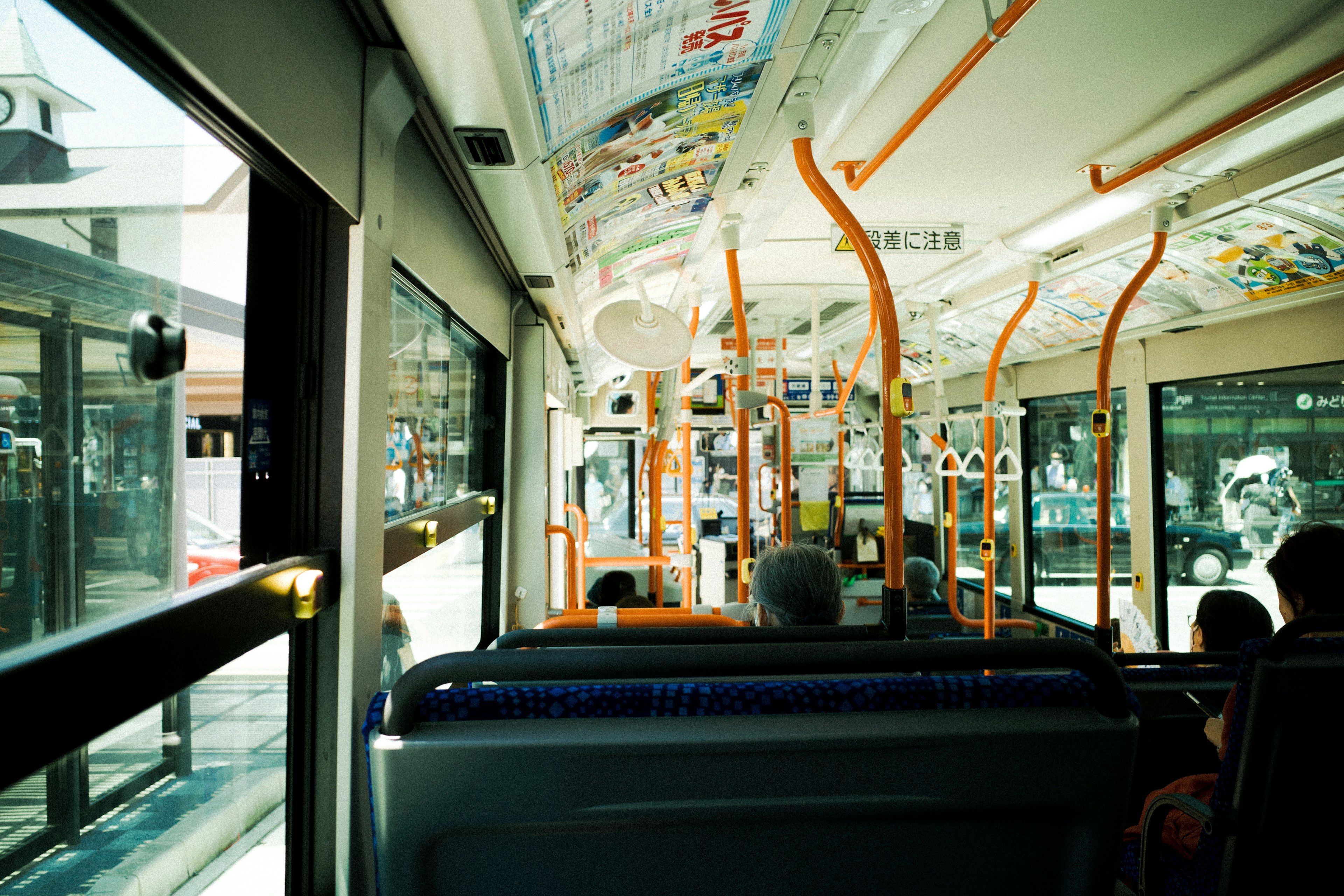 Interior view of a bus with bright natural light seating and orange handrails