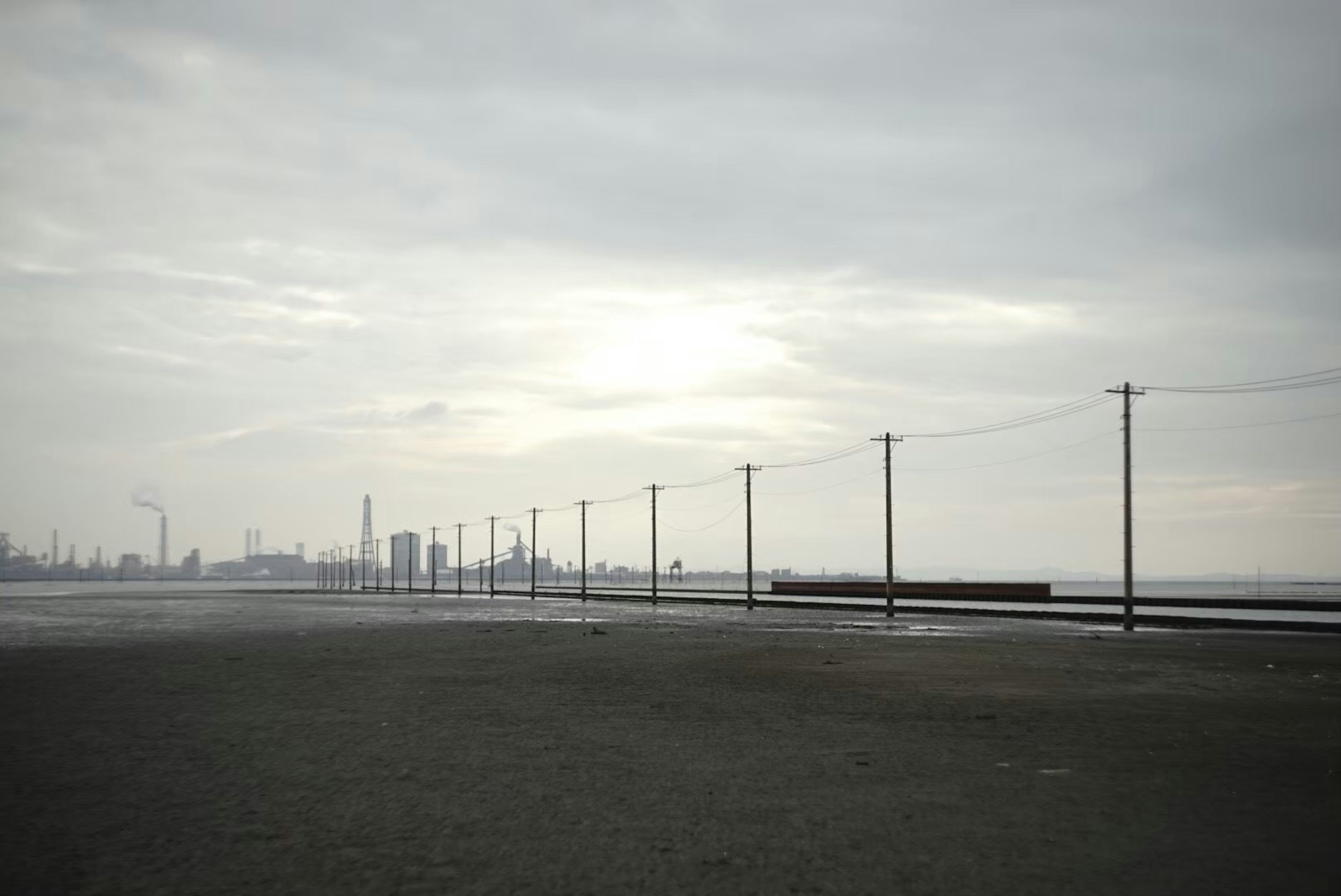 Industrial landscape under cloudy sky with power poles and factory silhouettes in the background