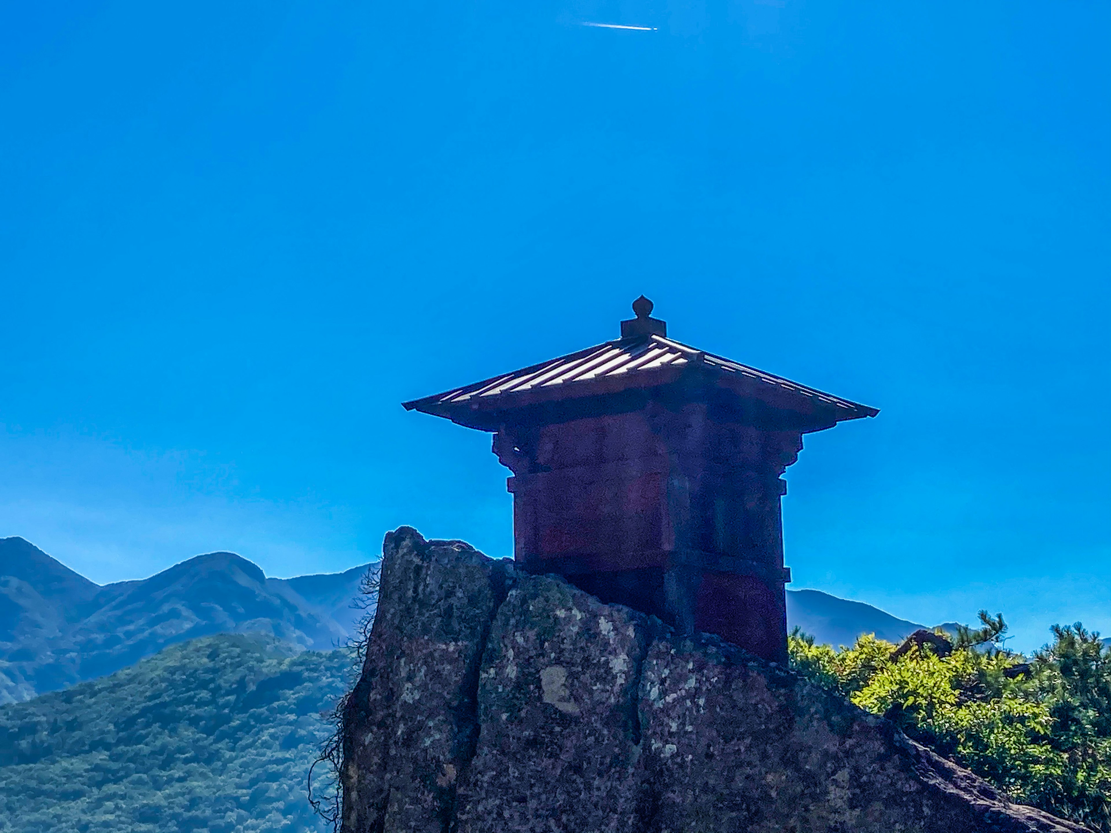 Red structure perched on a rock under a clear blue sky with mountains in the background