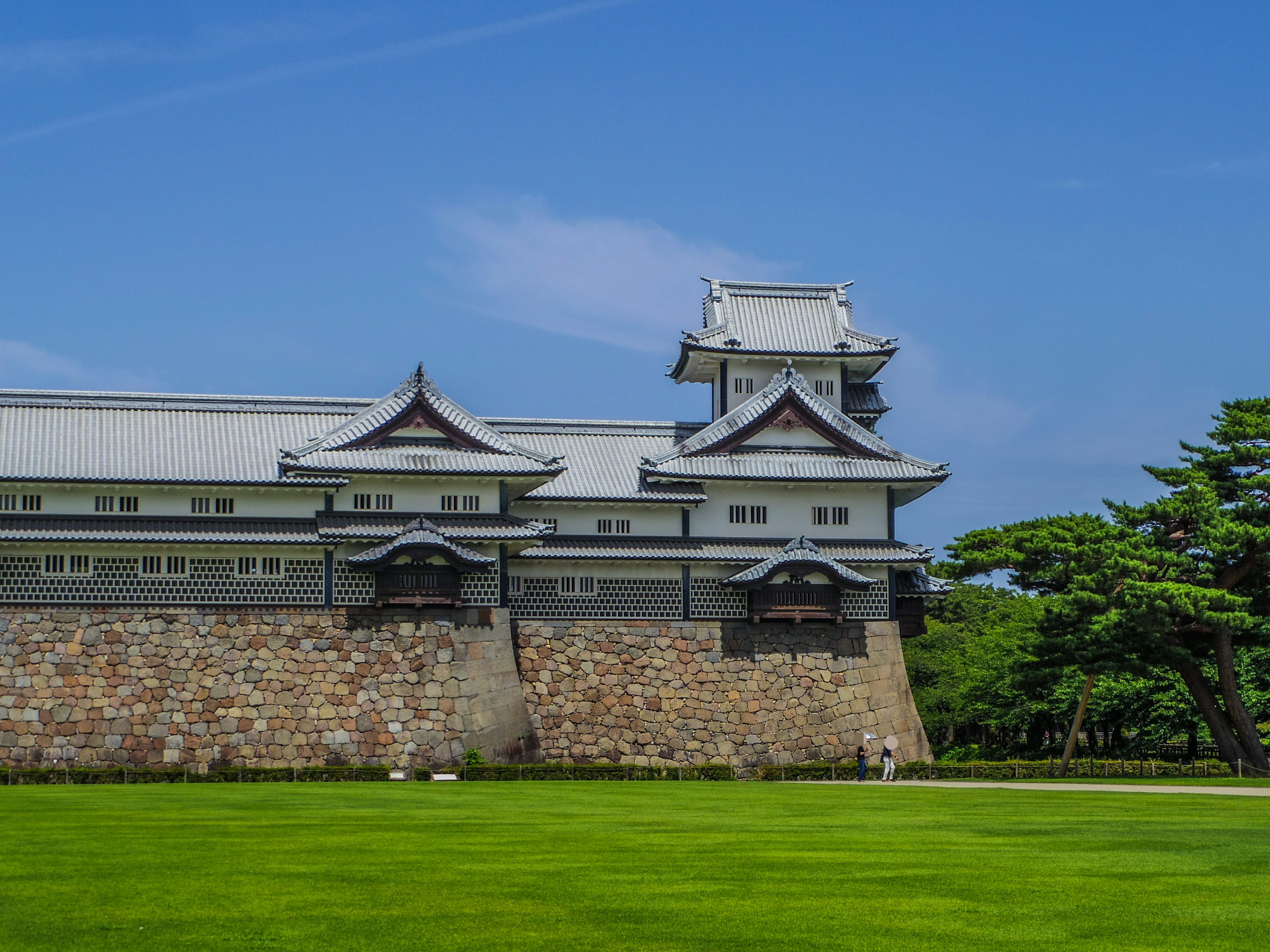 青空の下にある伝統的な日本の城の一部と緑の芝生