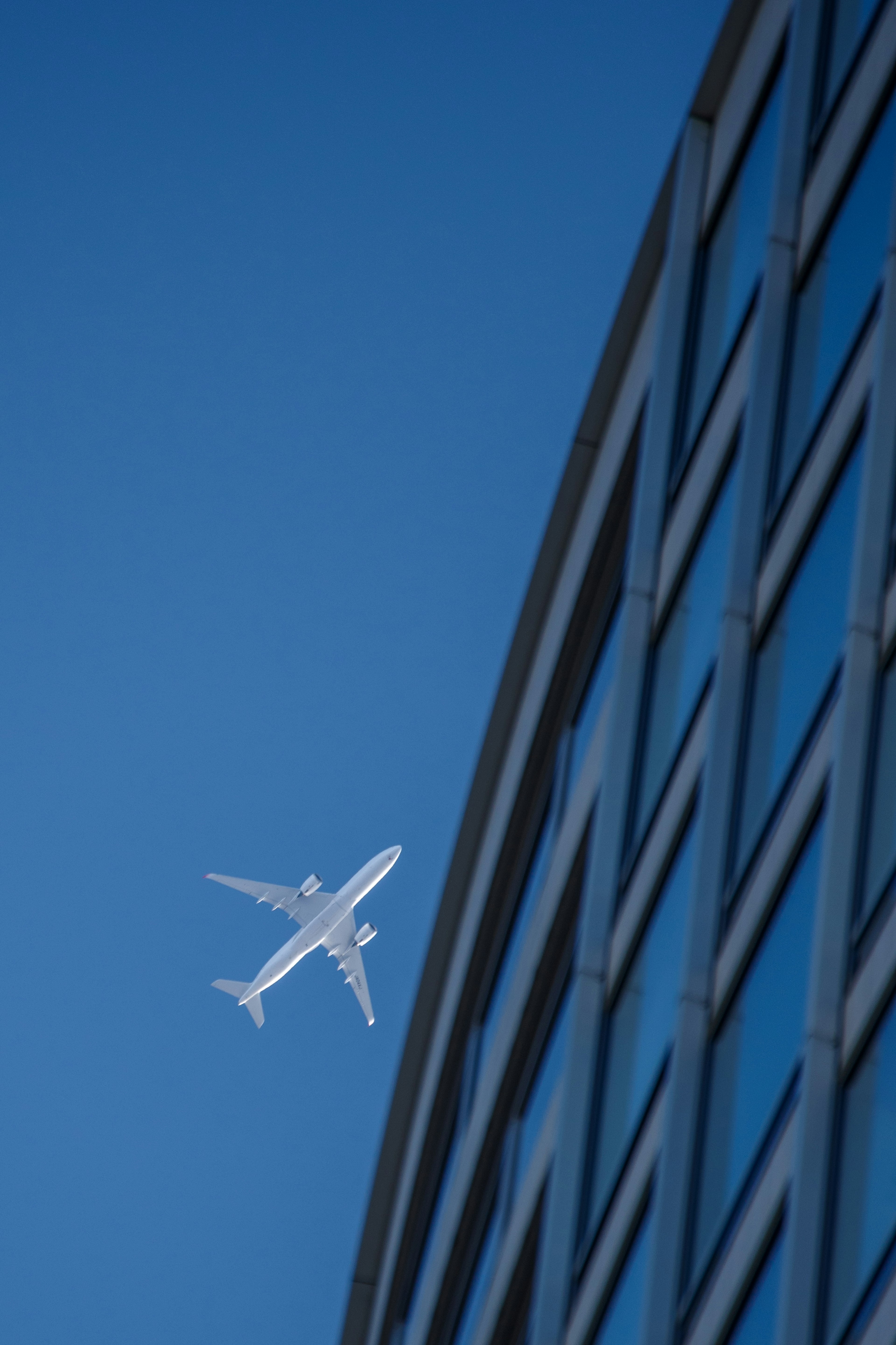 Airplane flying in blue sky near glass building