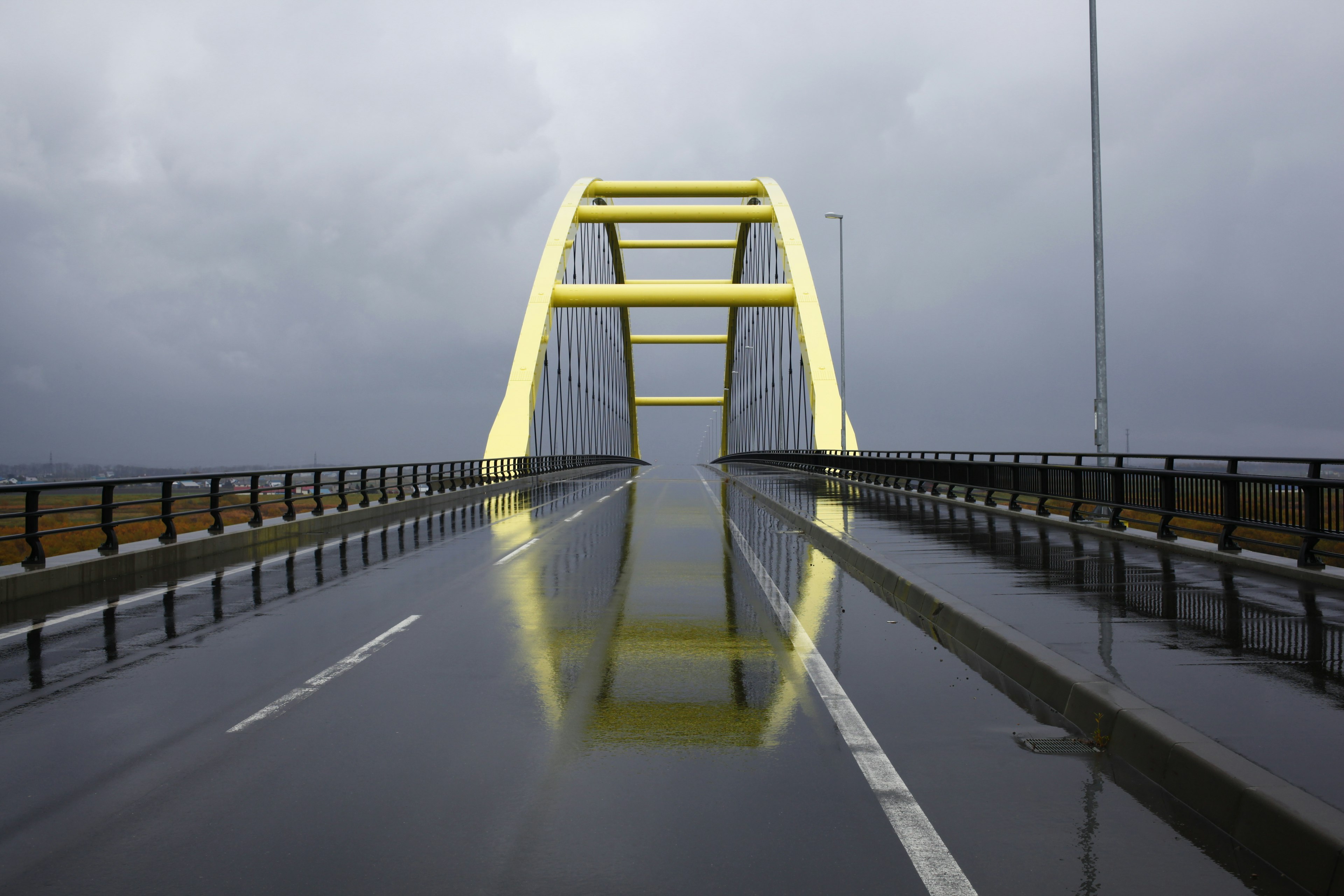 Pont en arc jaune se reflétant dans des flaques sur une route mouillée