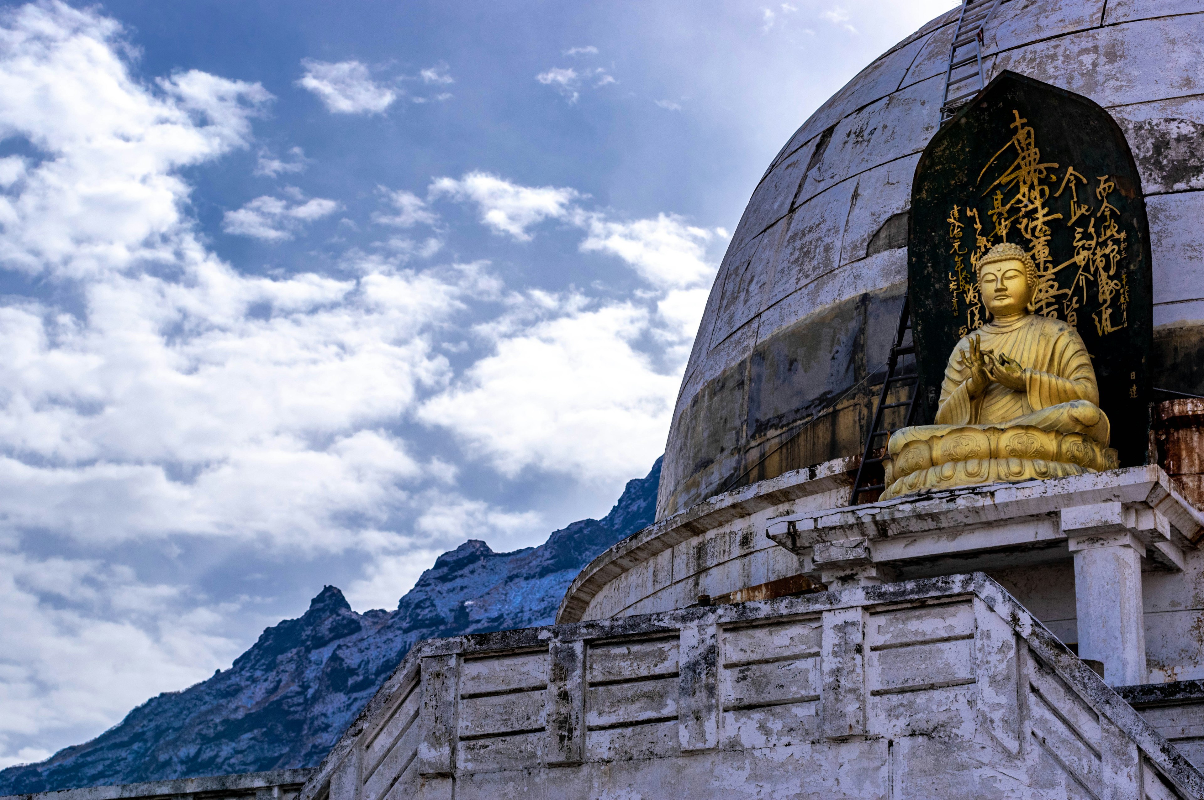 Statua del Buddha dorato presso uno stupa con sfondo montano